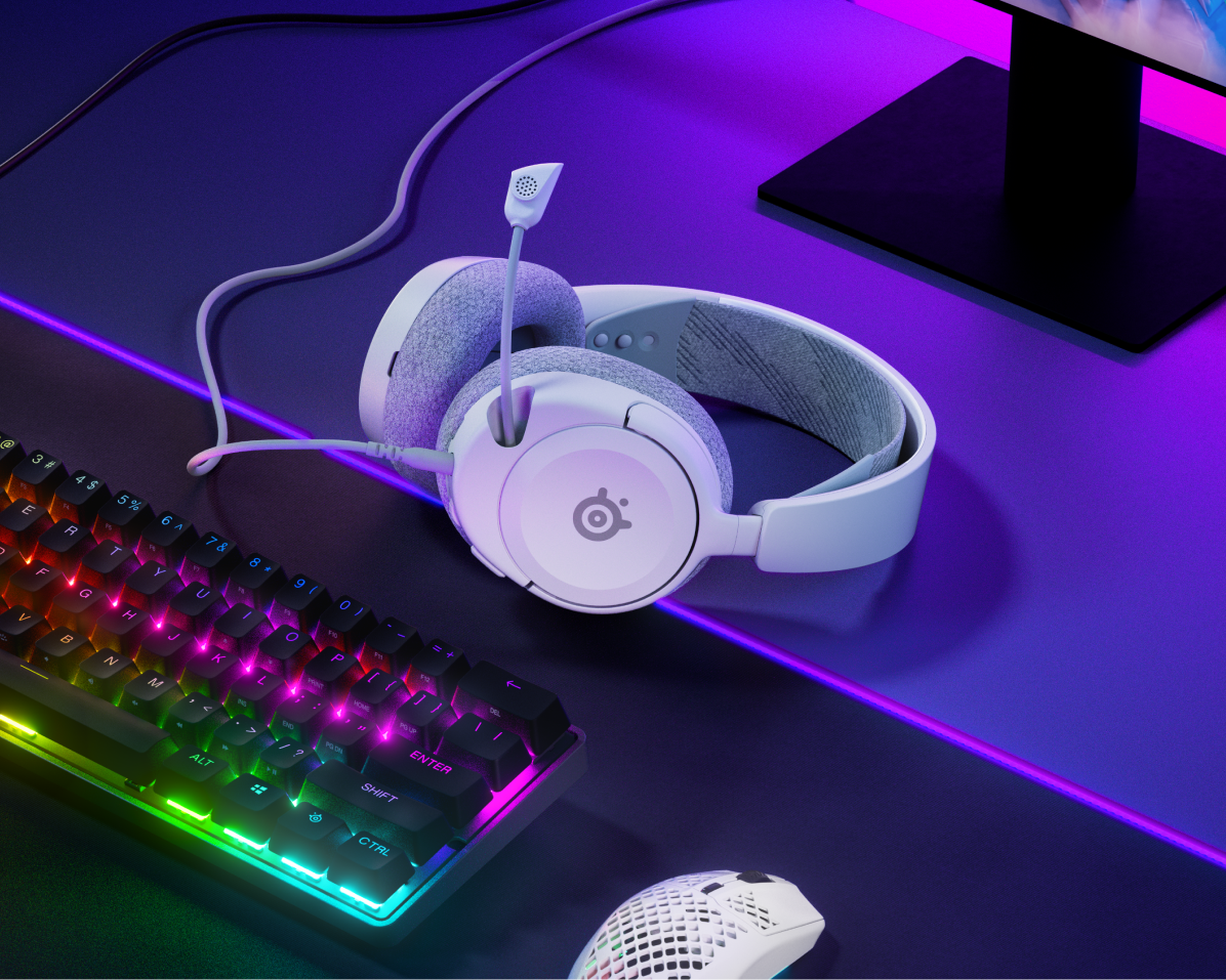 Cuffie, tastiera con luci arcobaleno e un mouse bianco sulla scrivania.