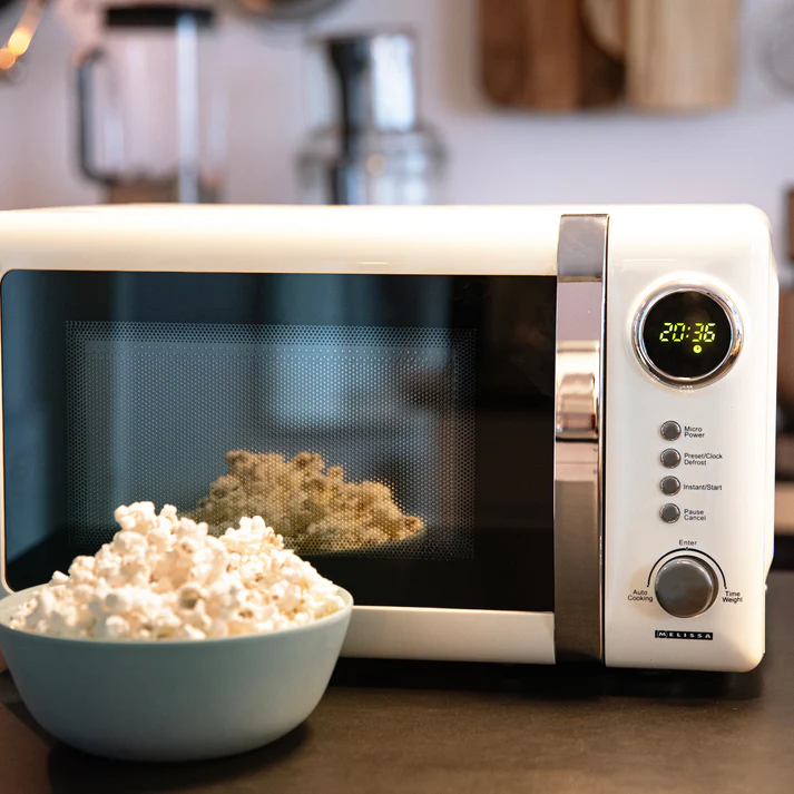 Micro-ondes blanc avec un bol de pop-corn devant, l'affichage de l'heure allumé à 20h36.