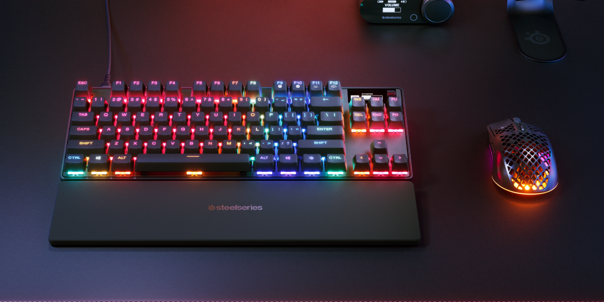 RGB-beleuchtete Tastatur mit Handgelenkauflage und Maus auf einem Schreibtisch.