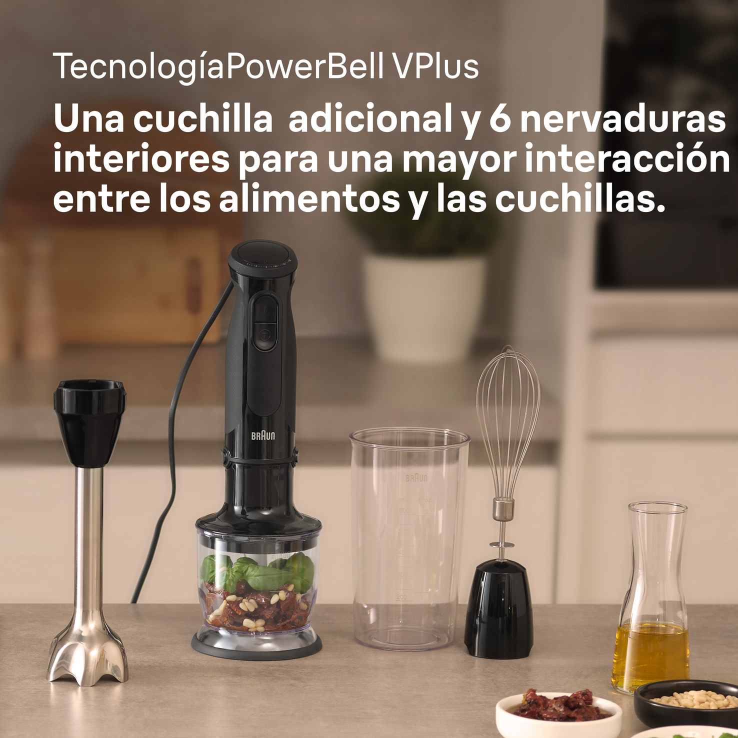 Batidora de mano negra con accesorios, albahaca, tomates, aceite y cuencos sobre una mesa.