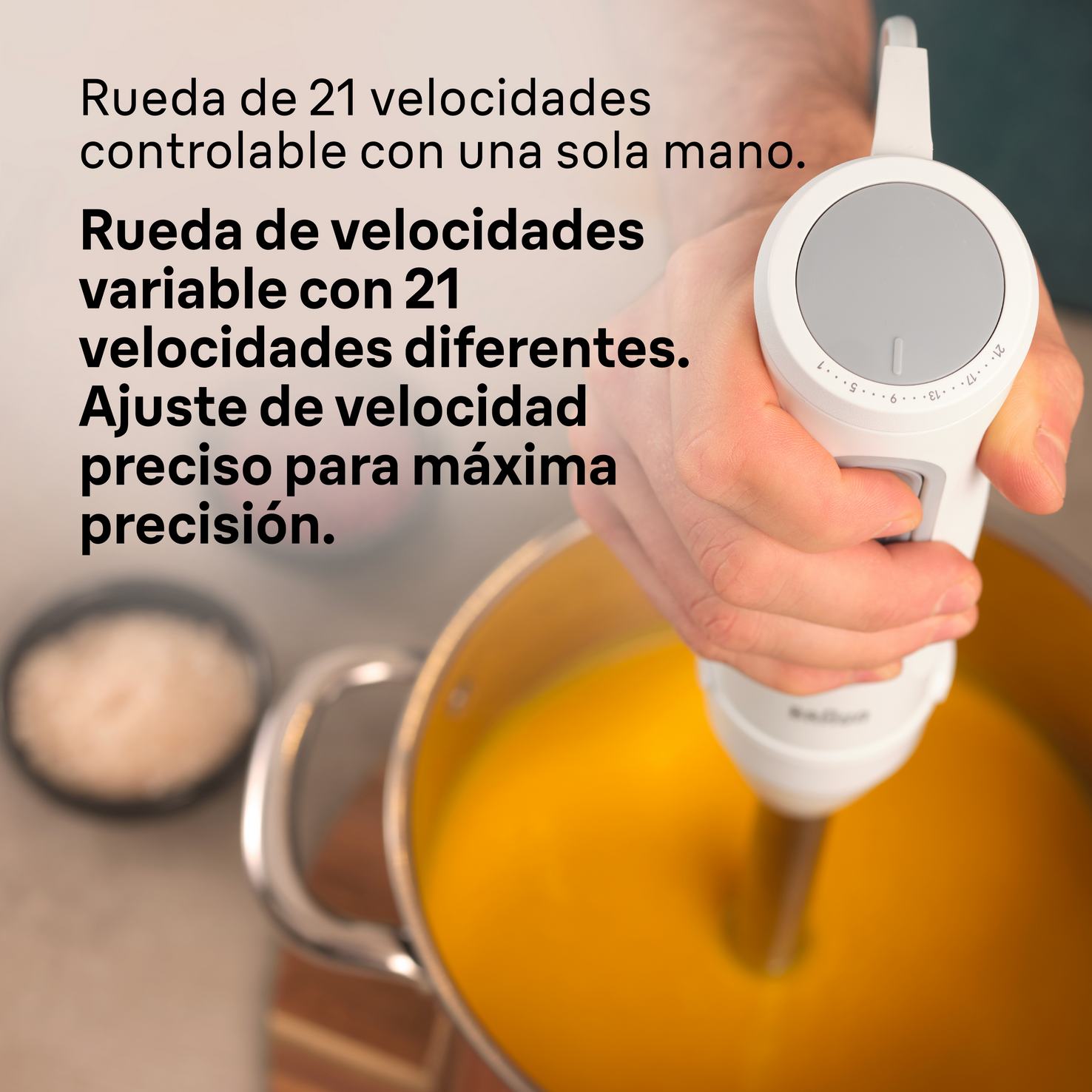 Mano sostiene batidora de inmersión sobre sopa, ajustes de velocidad visibles.