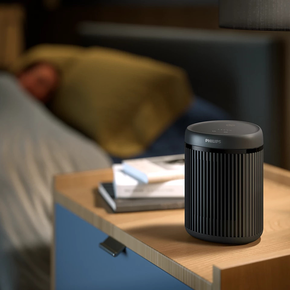 Czarny oczyszczacz powietrza Philips na stoliku nocnym z osobą w łóżku.