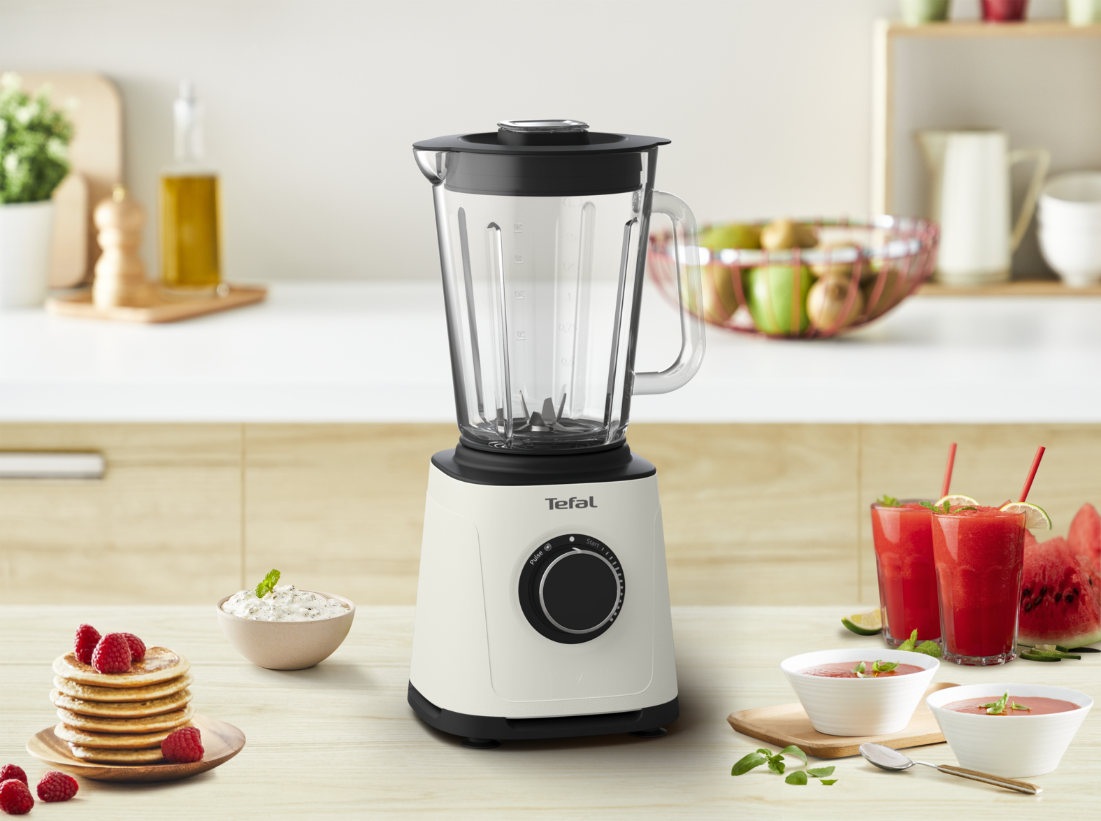 Egy fehér Tefal turmixgép, smoothie-összetevőkkel és egy rakás palacsintával egy fa felületen.