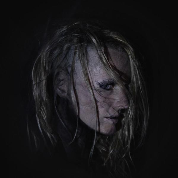 Gesicht einer Frau im Schatten, blondes Haar, dunkler Hintergrund.