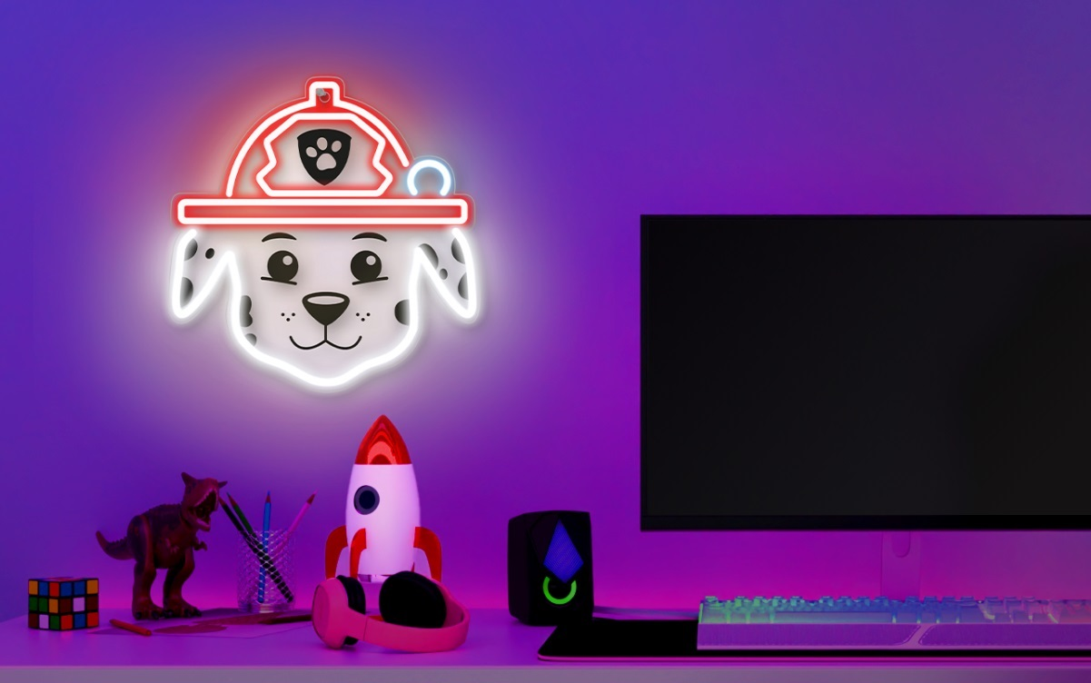 Neonowy znak psa Marshalla. Na biurku znajdują się komputer, słuchawki i zabawki. Tło jest fioletowe.