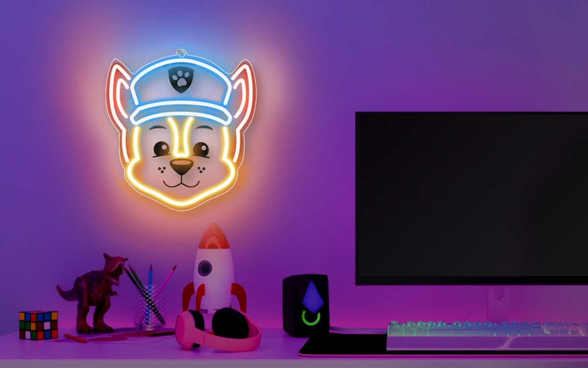 Neonowy znak głowy psa z kreskówki. Poniżej na biurku znajdują się zabawki.