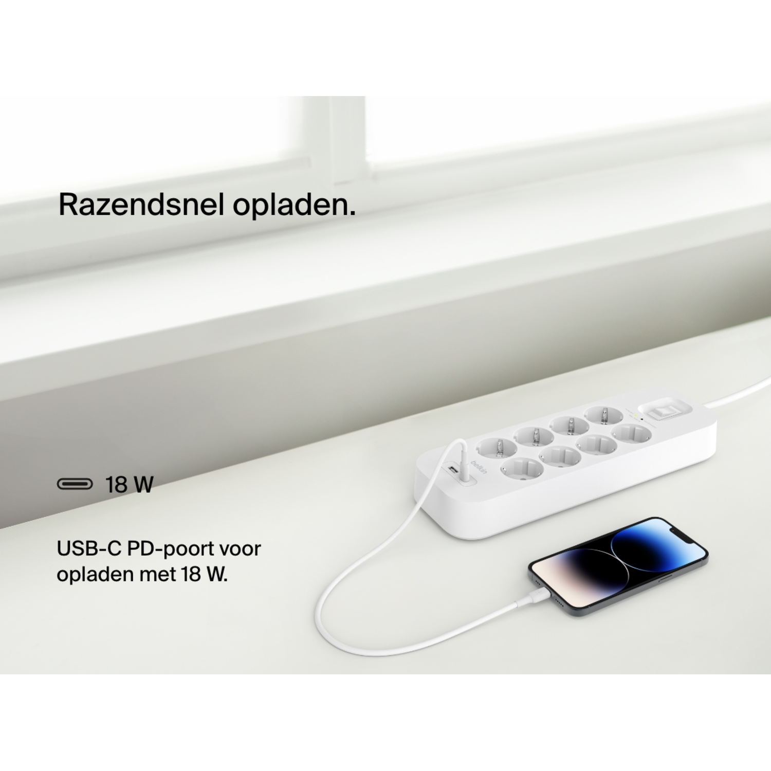 Een witte stekkerdoos met een telefoon die via USB-C oplaadt, op een wit oppervlak.