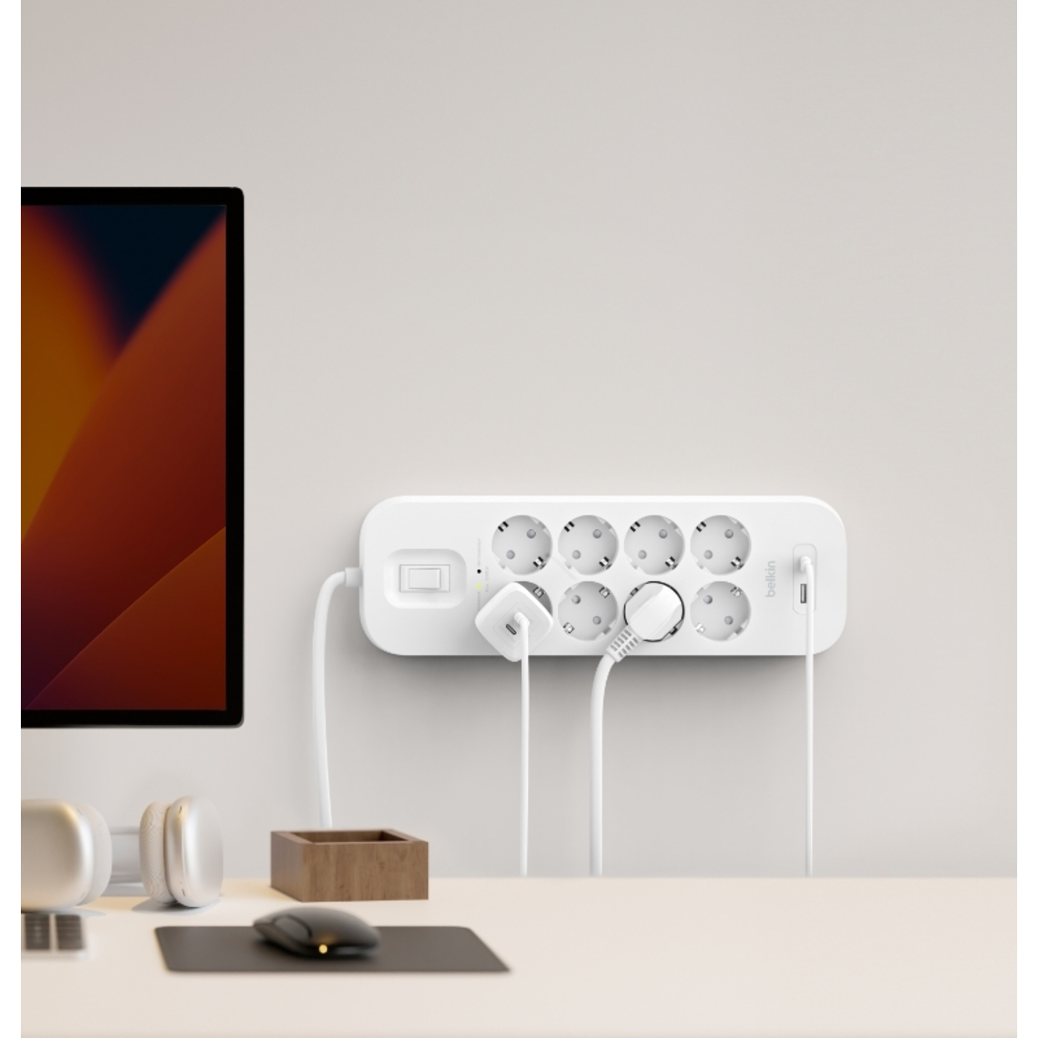 Witte Belkin stekkerdoos met meerdere stopcontacten en aangesloten stekkers, aan een muur.