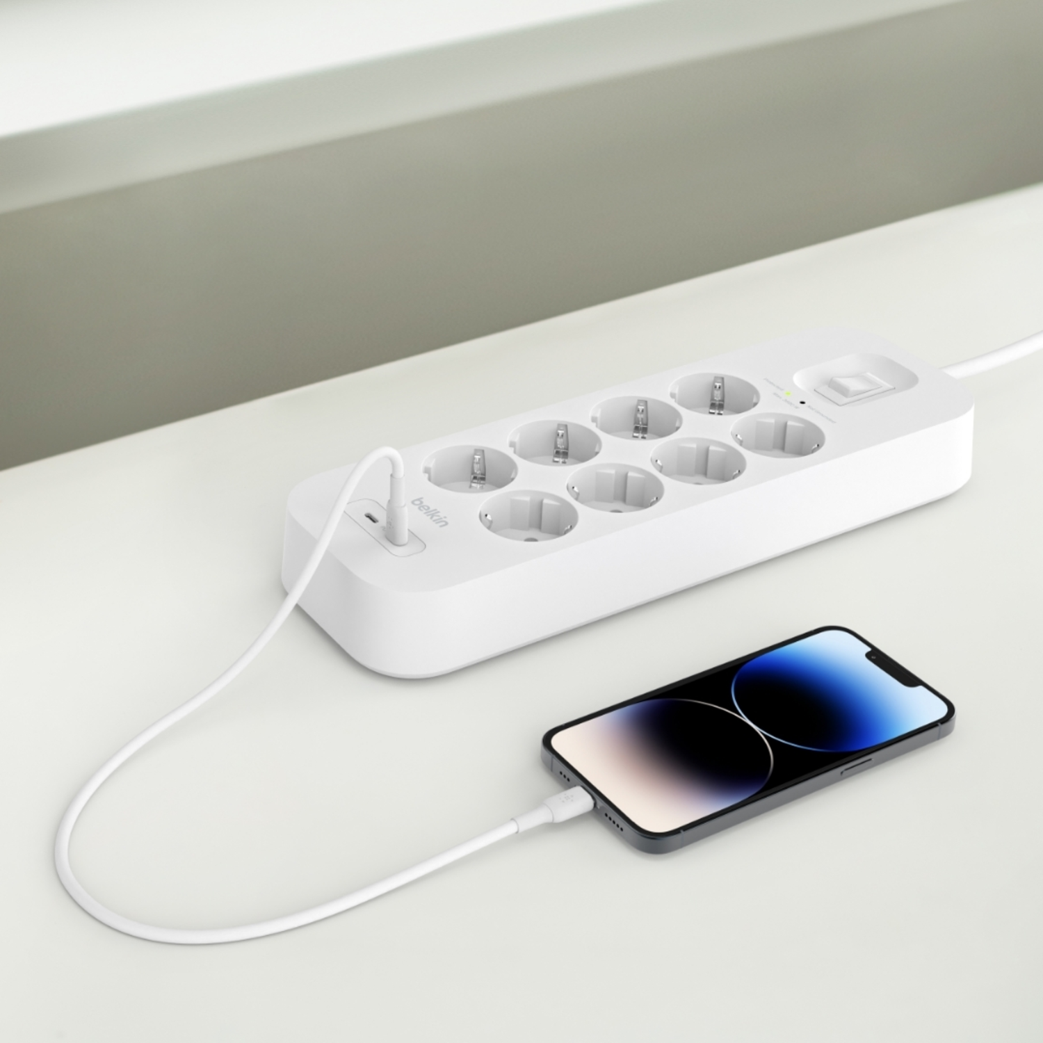 Witte stekkerdoos met meerdere stopcontacten, een aan/uit-knop en een telefoon die oplaadt.