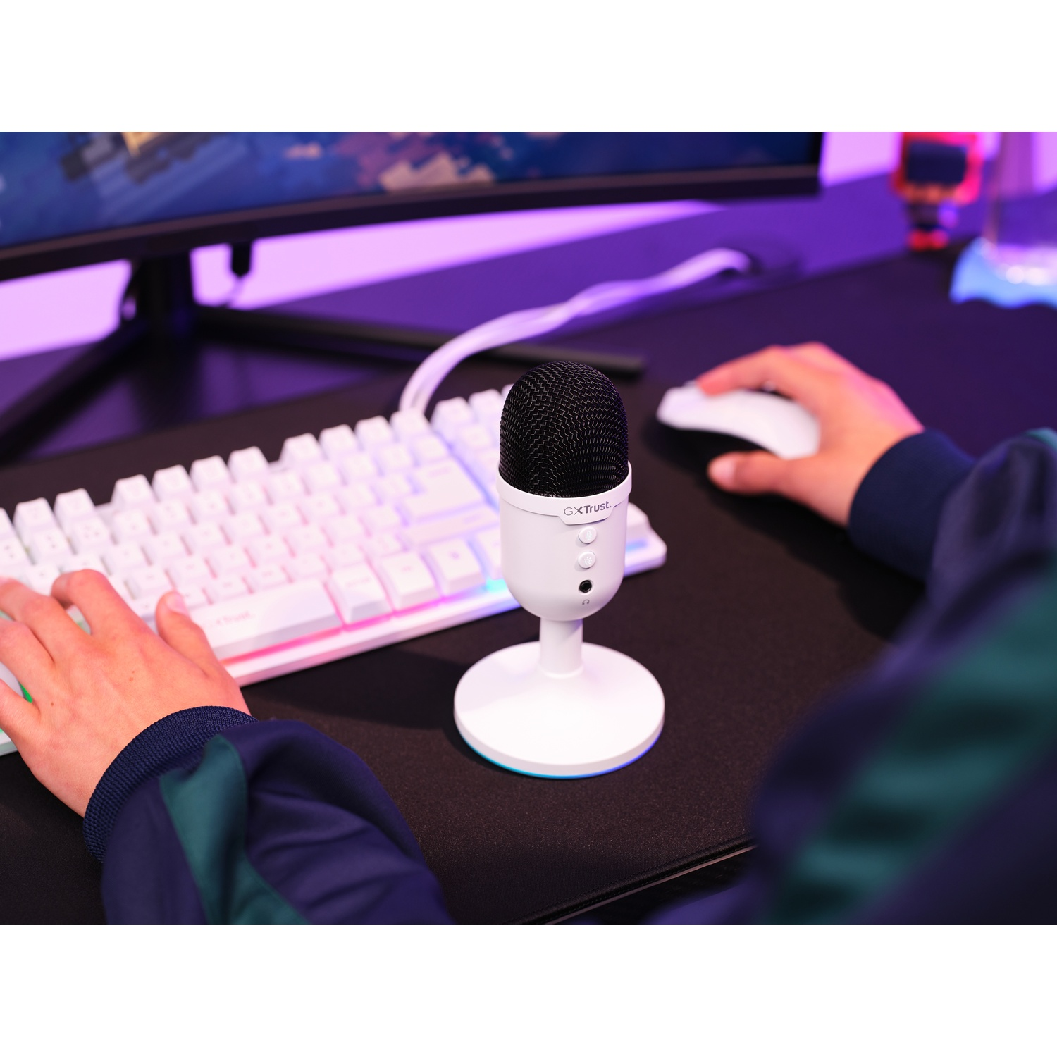 Microfono bianco su supporto. Tastiera, mouse e monitor sullo sfondo. Illuminazione viola.