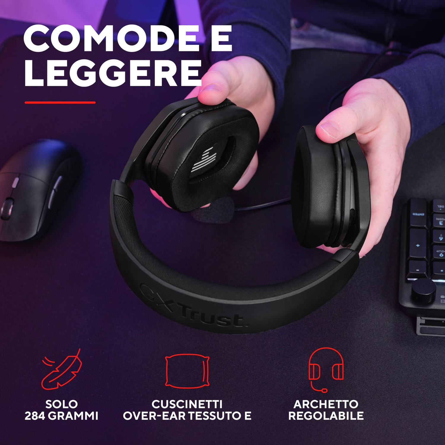 Persona che tiene cuffie nere, con mouse e tastiera sullo sfondo.