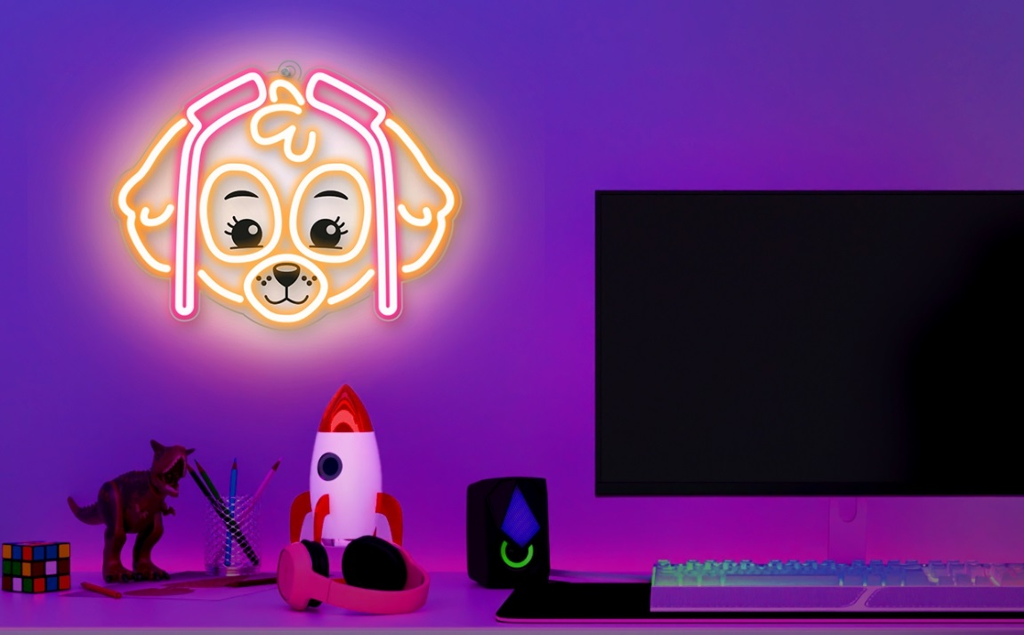 Neonowy znak psa nad biurkiem z komputerem i innymi przedmiotami. Scena jest fioletowa i różowa.