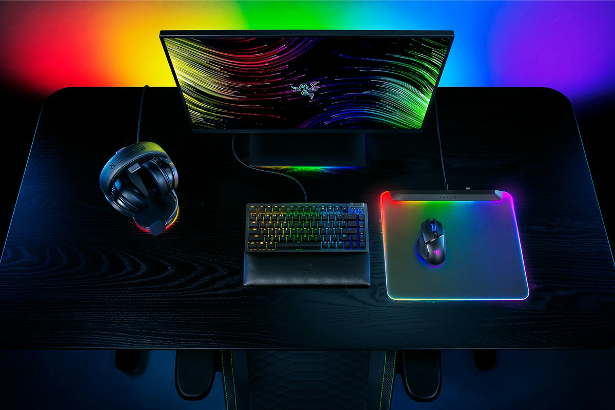 Ein Gaming-Setup mit Monitor, Tastatur, Maus und Headset. Schreibtisch und Zubehör haben RGB-Beleuchtung.