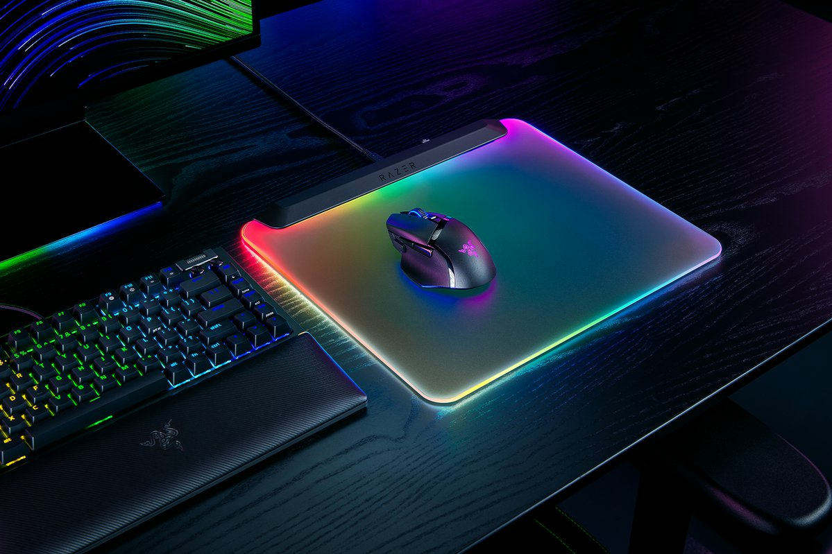 Gaming-Maus auf einem regenbogenfarbenen Mauspad, Tastatur im Vordergrund. Dunkler Schreibtisch.