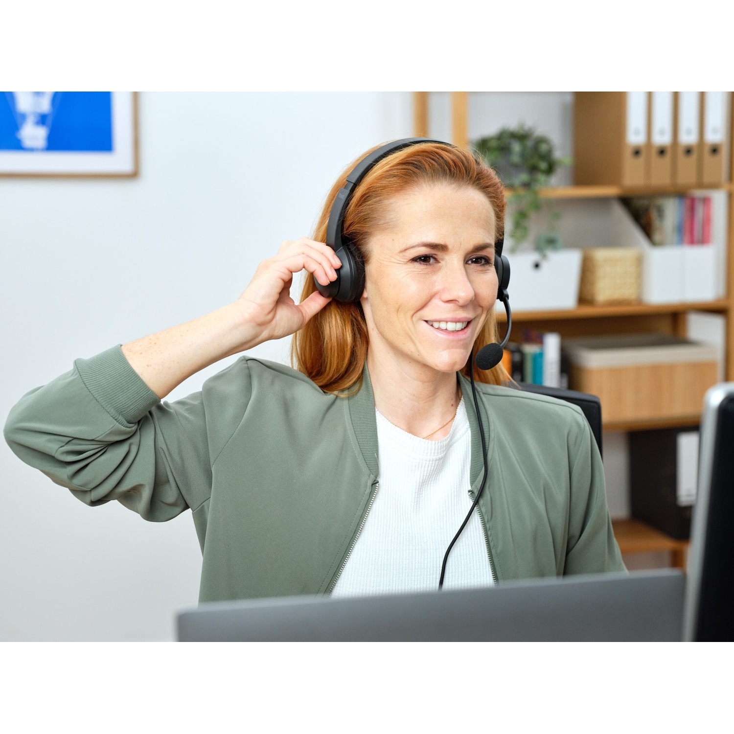 Donna con i capelli rossi che indossa un auricolare, sorridendo mentre guarda il computer.
