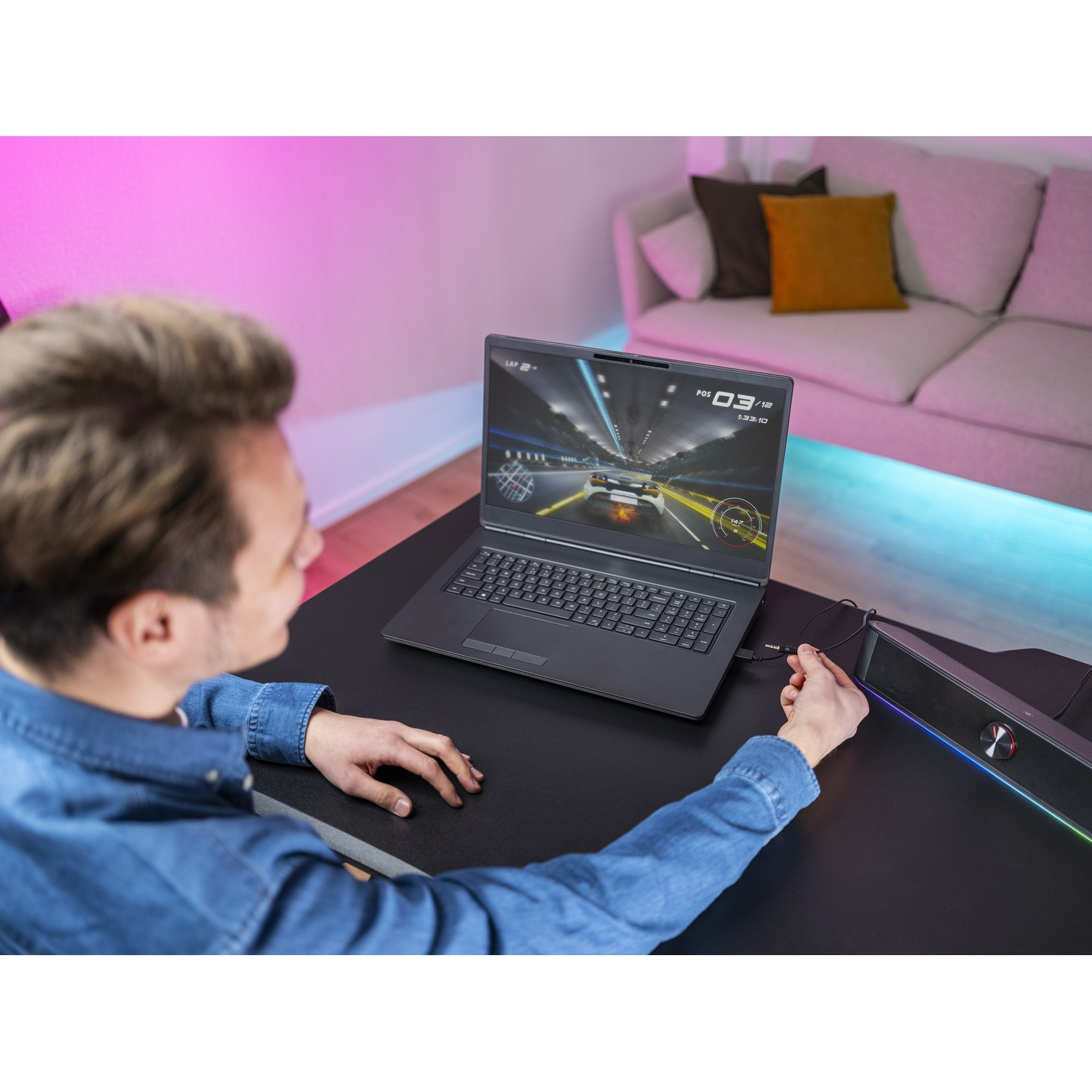 Uomo che gioca a un gioco di corse su un laptop a una scrivania. Un altoparlante è collegato. Un divano è sullo sfondo.