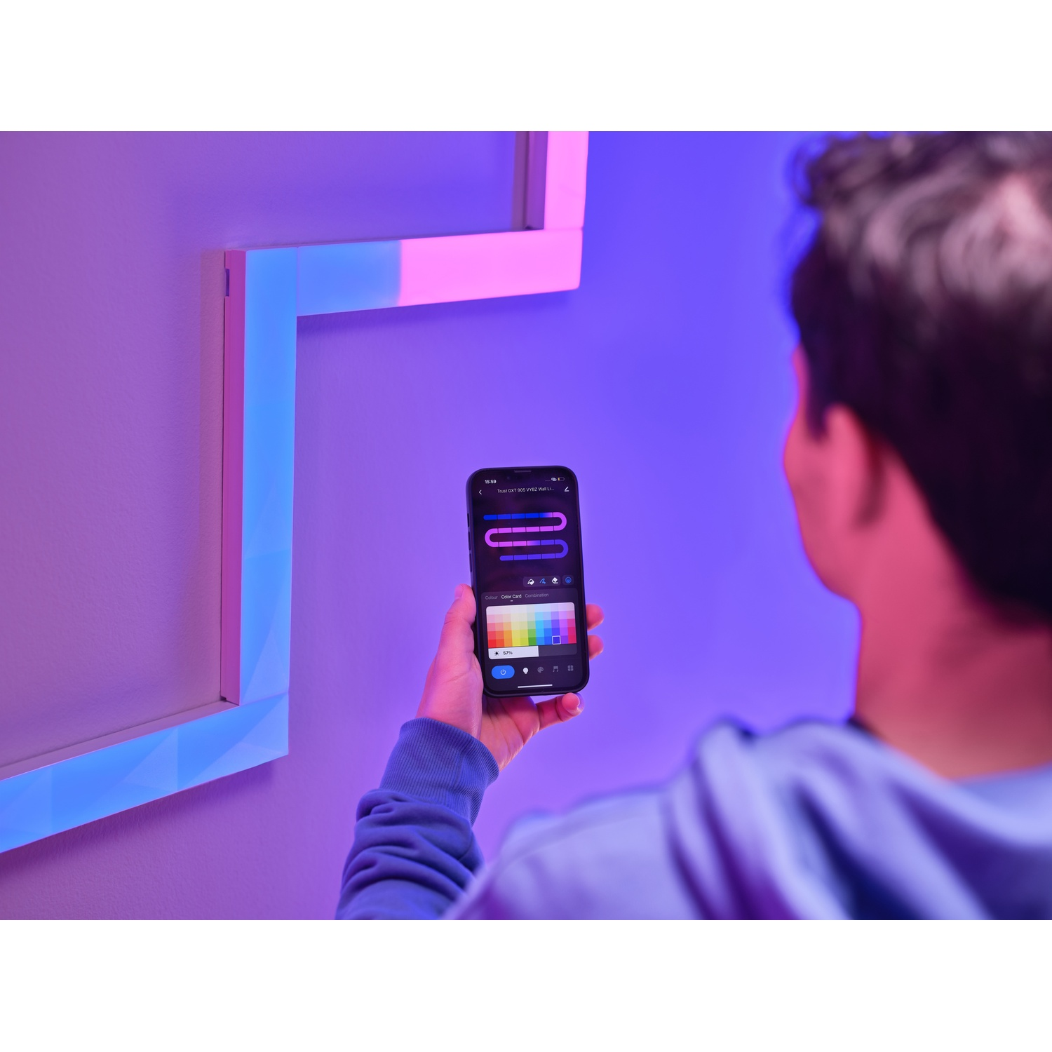 Persona con telefono, controlla luci smart home. Display luminoso colorato sul muro.