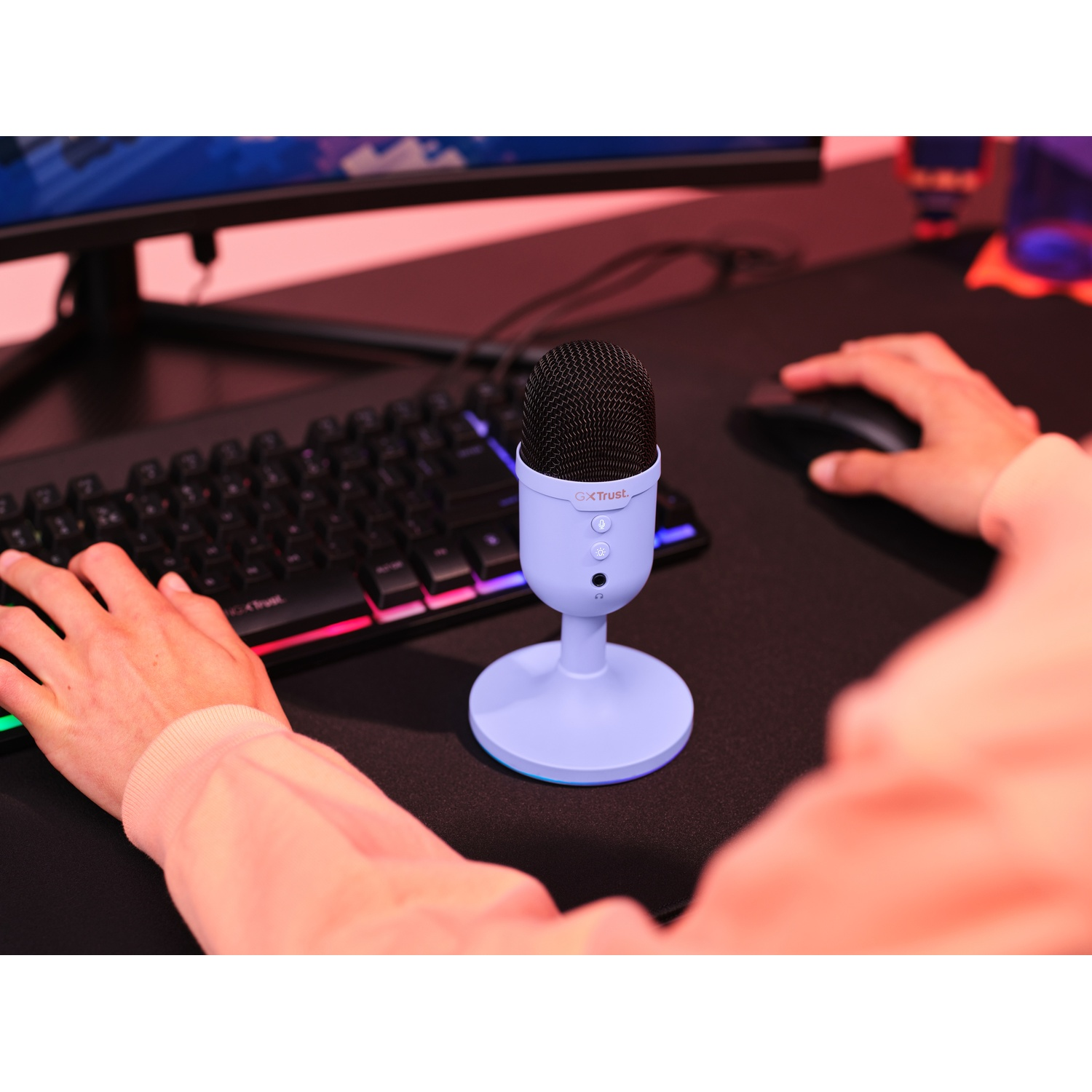 Microfono su un supporto, tastiera, mouse e mani davanti a un monitor.