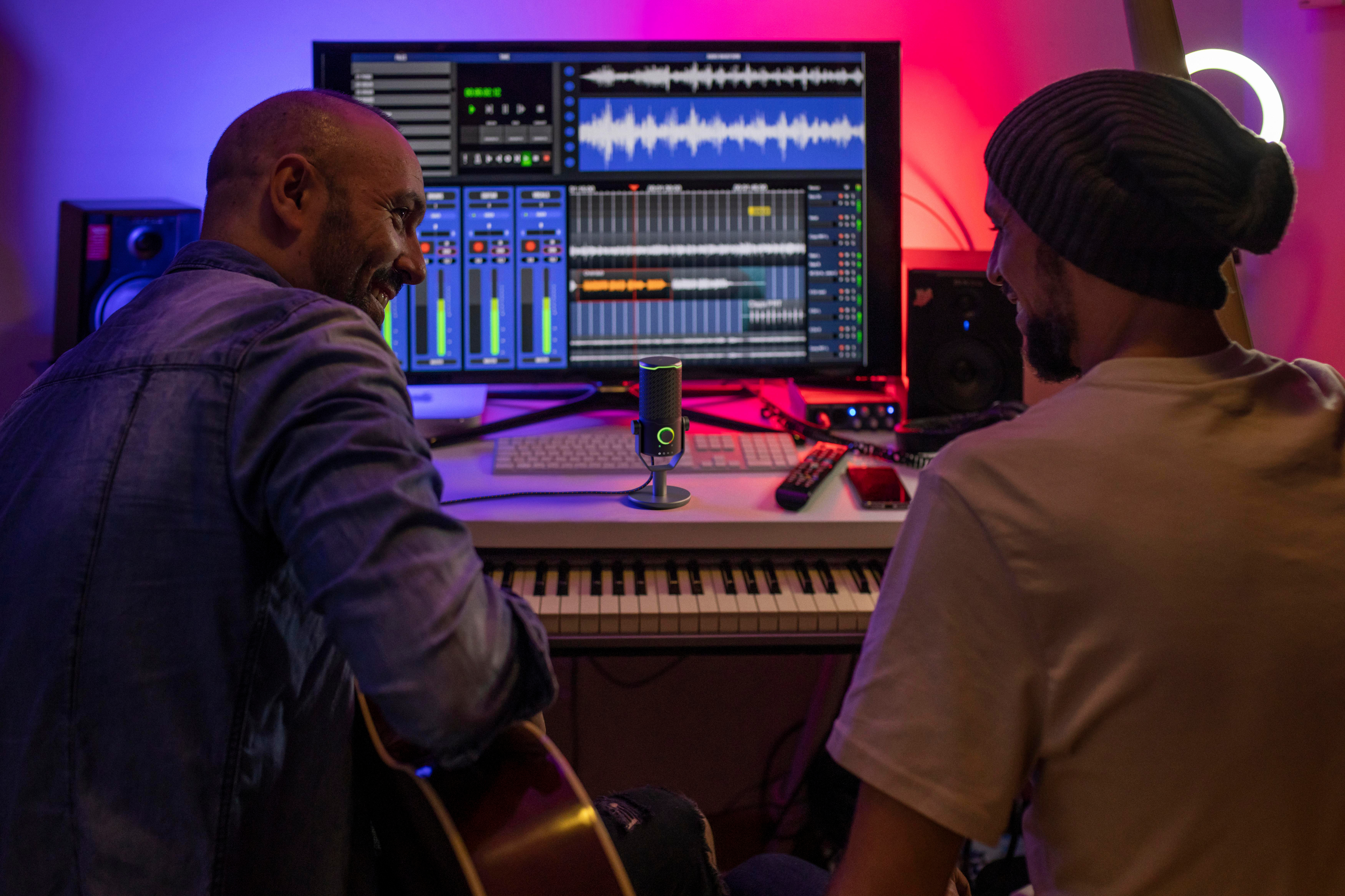 Zwei Männer in einem Aufnahmestudio; einer spielt Gitarre, der andere schaut auf einen Bildschirm.