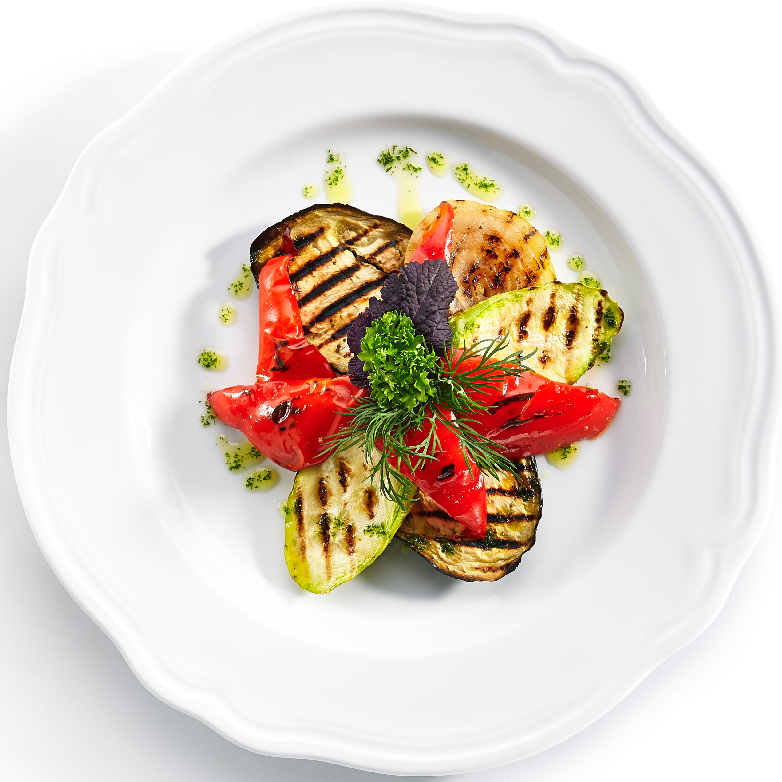 Légumes grillés disposés sur une assiette blanche avec des herbes et de l'huile.