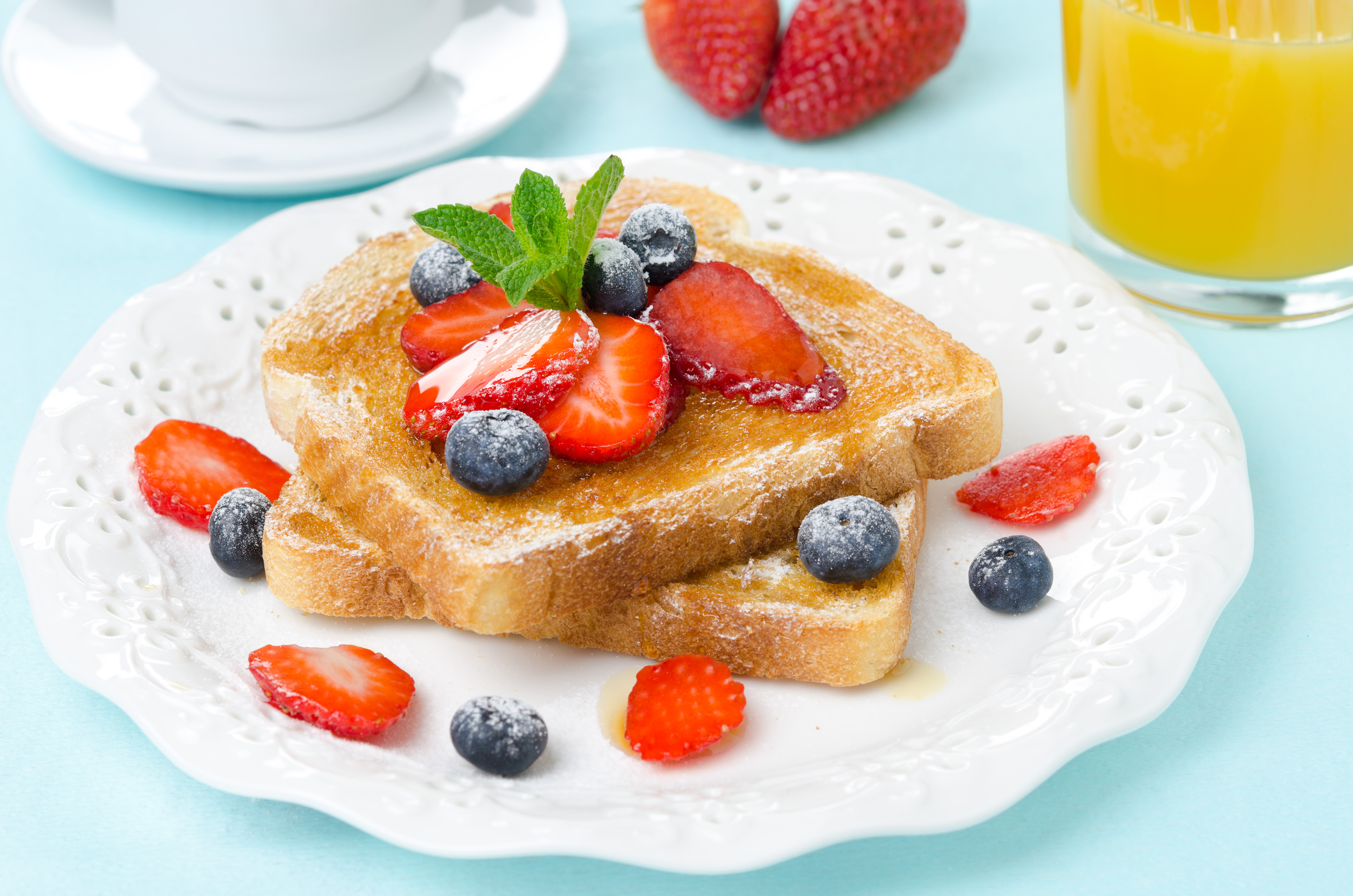 Toast de petit-déjeuner avec des baies et de la menthe sur une assiette blanche. Jus d'orange et café en arrière-plan.