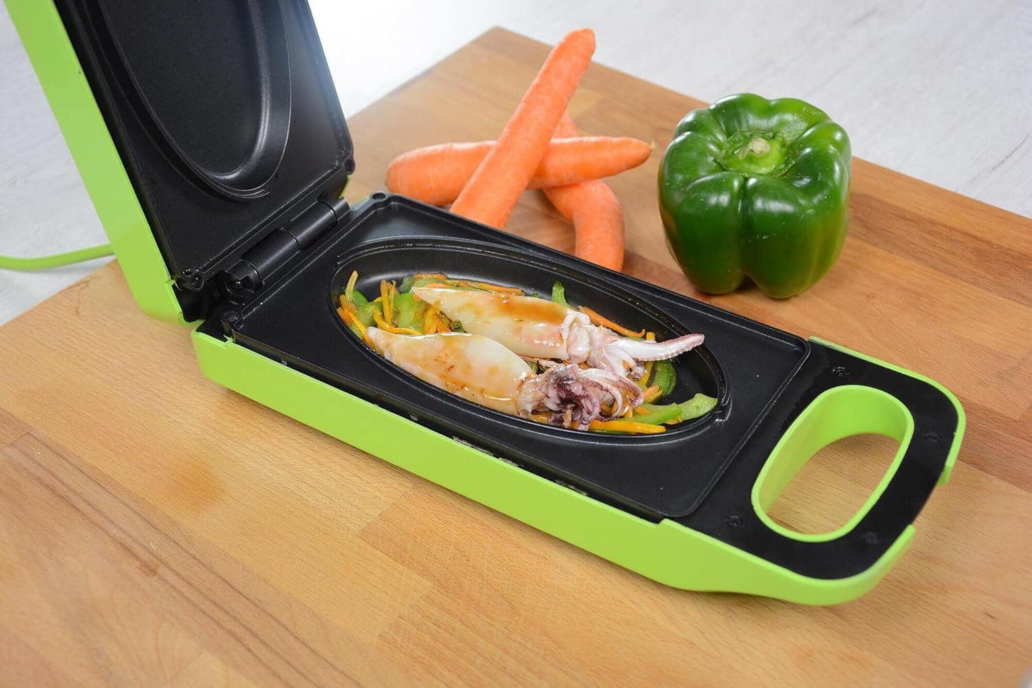 Piastra elettrica verde con calamari cotti e verdure su una superficie di legno.