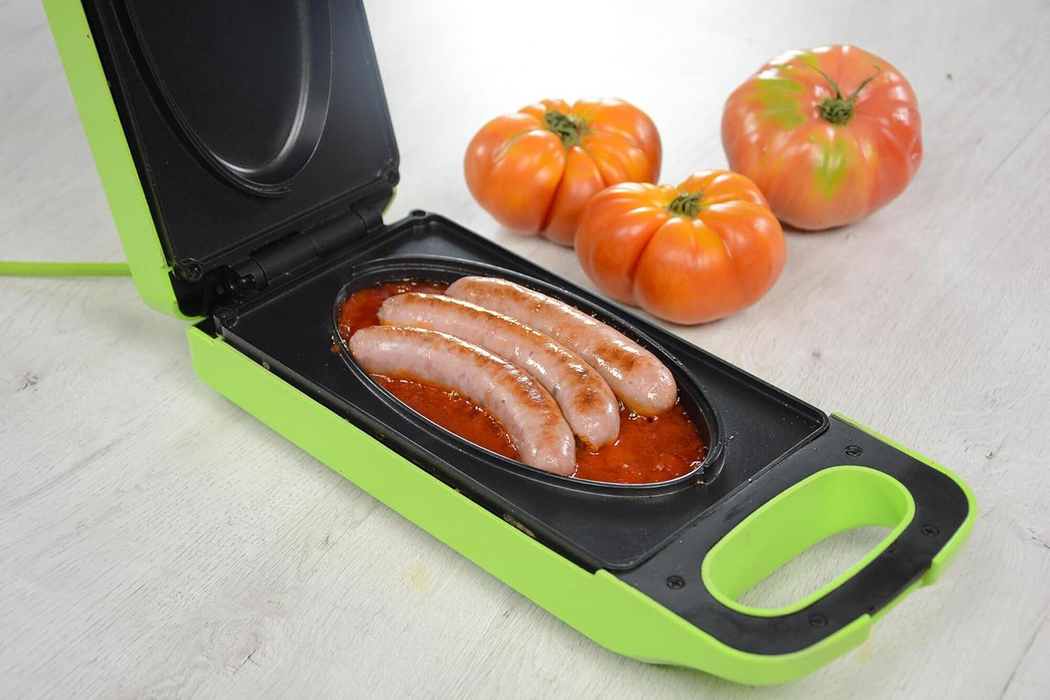 Griglia elettrica con salsicce e salsa, con pomodori a lato.