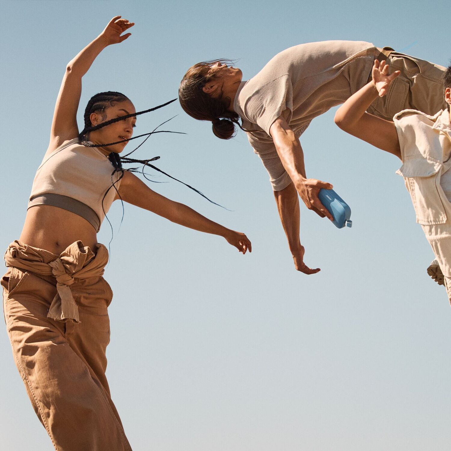Trois personnes dansant dans les airs contre un ciel bleu clair.