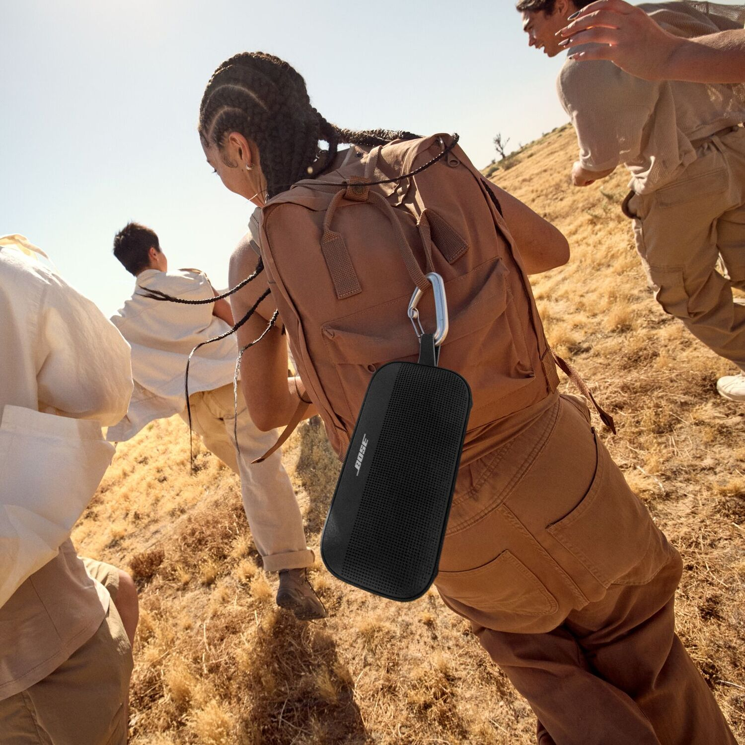 Des gens font de la randonnée au soleil, l'un d'eux porte un haut-parleur Bose noir attaché à un sac à dos.
