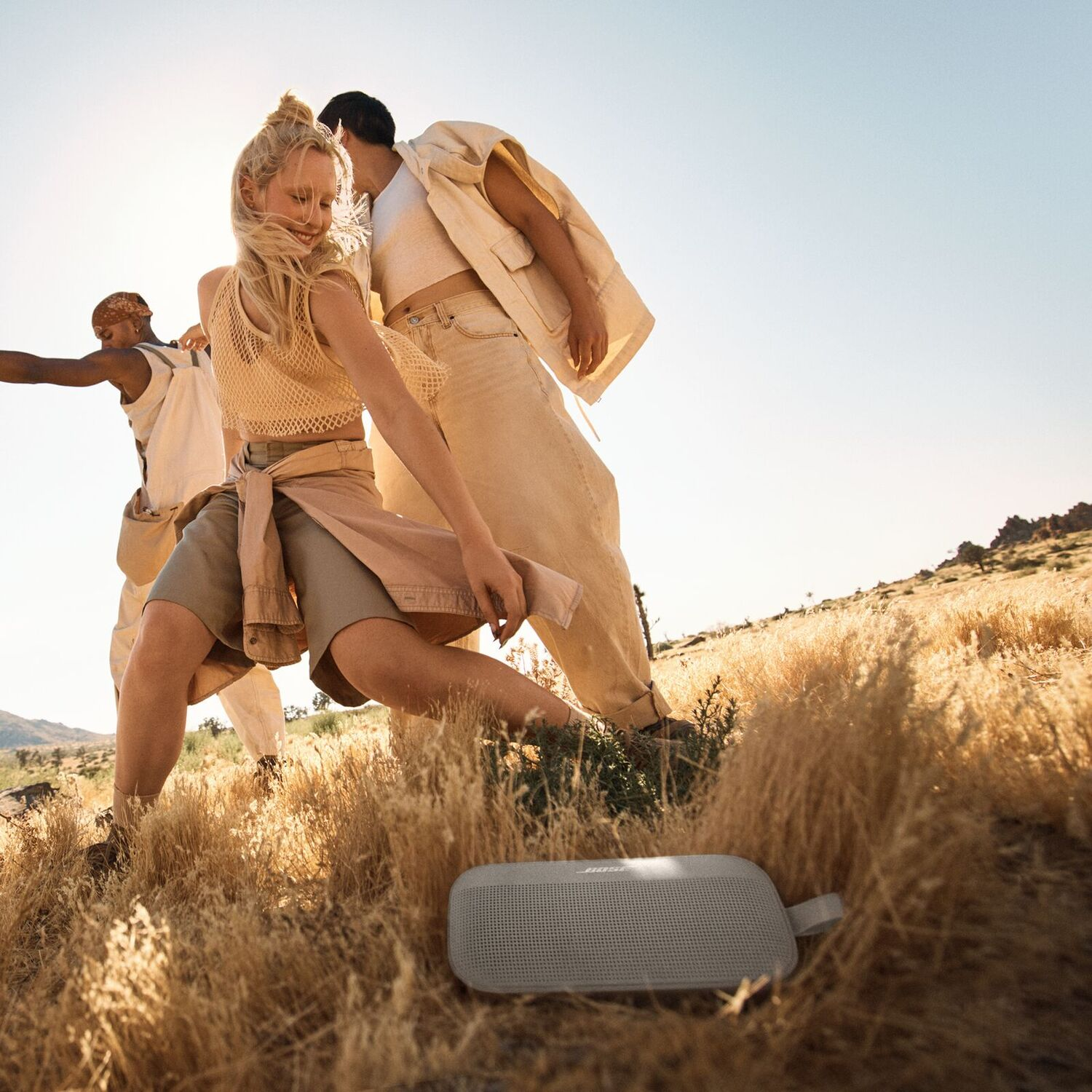People dancing in a field, Bose speaker in front, sunny day.