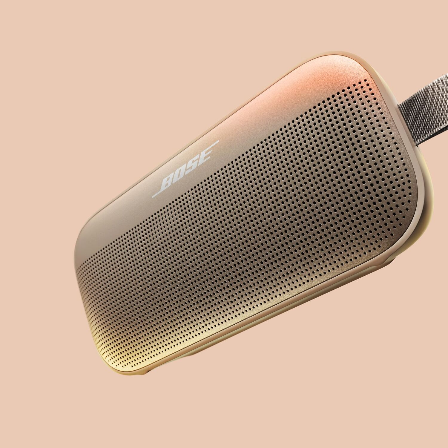 A gold colored rectangular Bose speaker on a peach background, with the Bose logo and a perforated surface.