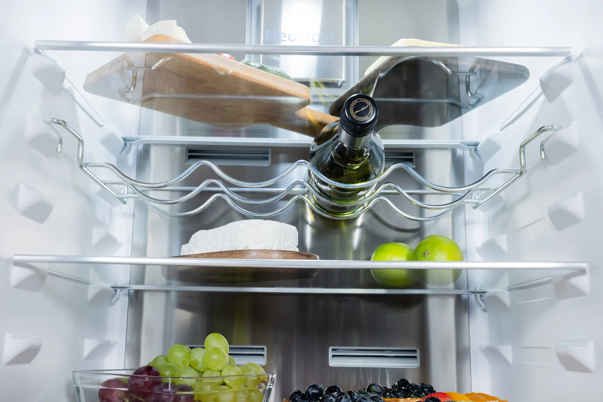 Wnętrze lodówki z półkami z żywnością: butelka wina, ser, owoce.