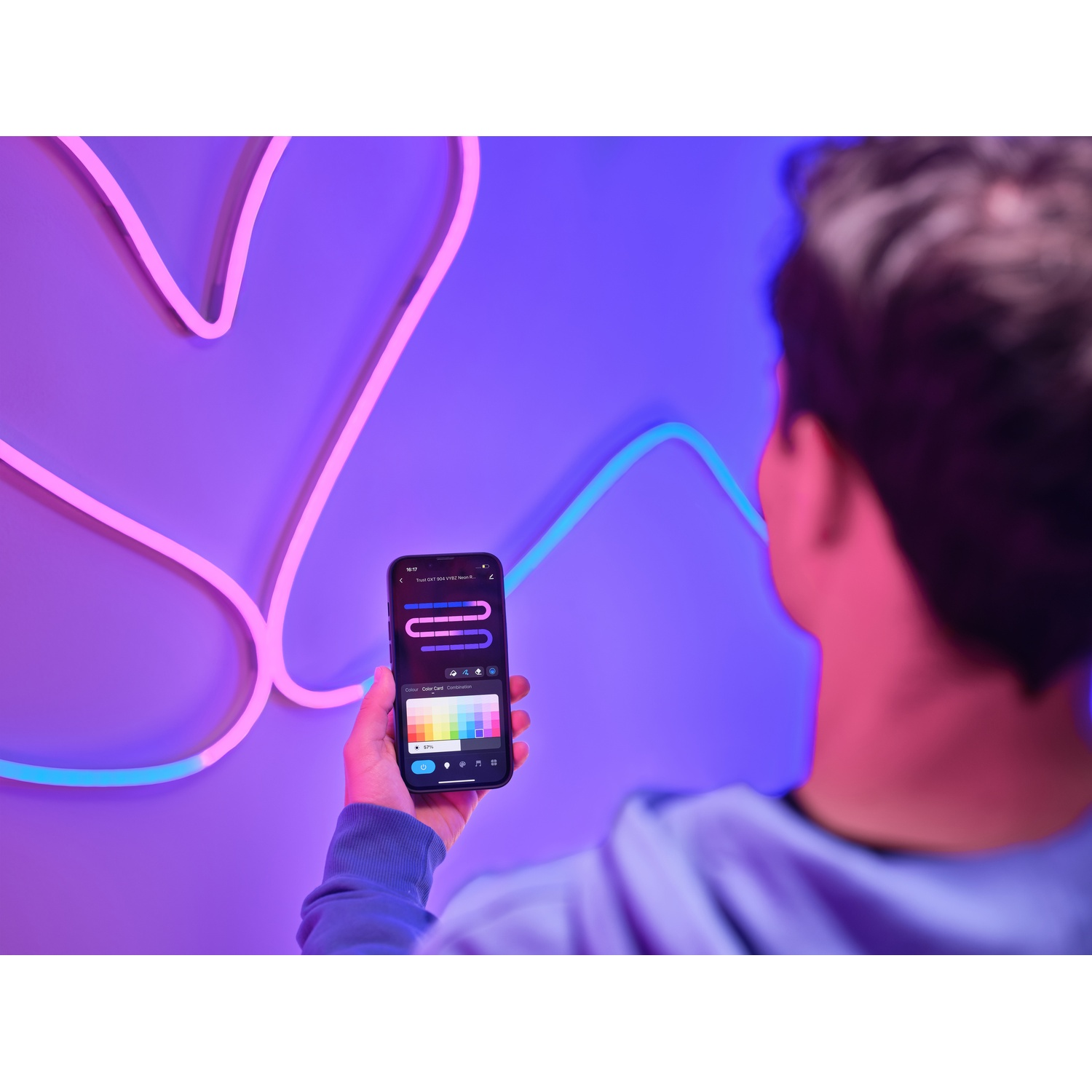 Persona che tiene in mano un telefono con un'app che controlla un'installazione di luci al neon. Luci al neon viola e blu.