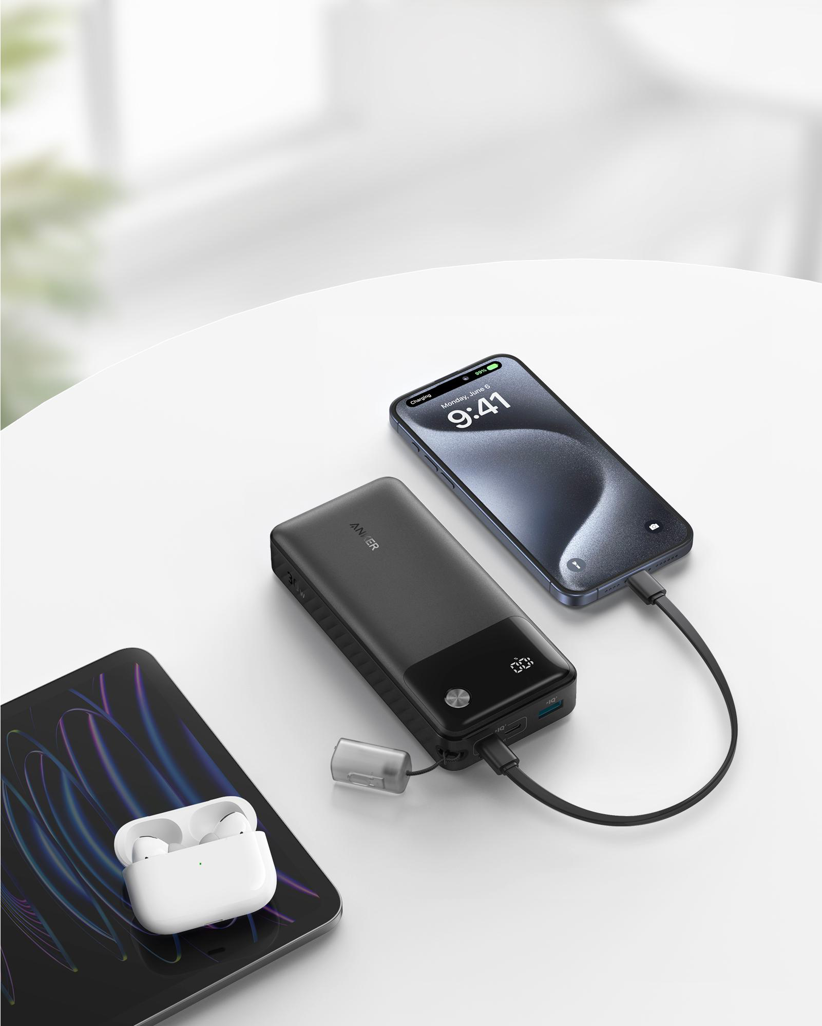 Schwarze Powerbank, die ein Telefon und ein Tablet auflädt. Ein Telefon zeigt 9:41 Uhr an. Weißer Tisch.