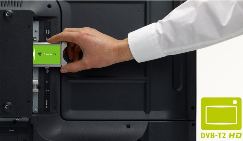 Eine Hand, die ein grünes freenetTV-Gerät in einen Fernseher einführt. Der Fernseher hat schwarze Anschlüsse.