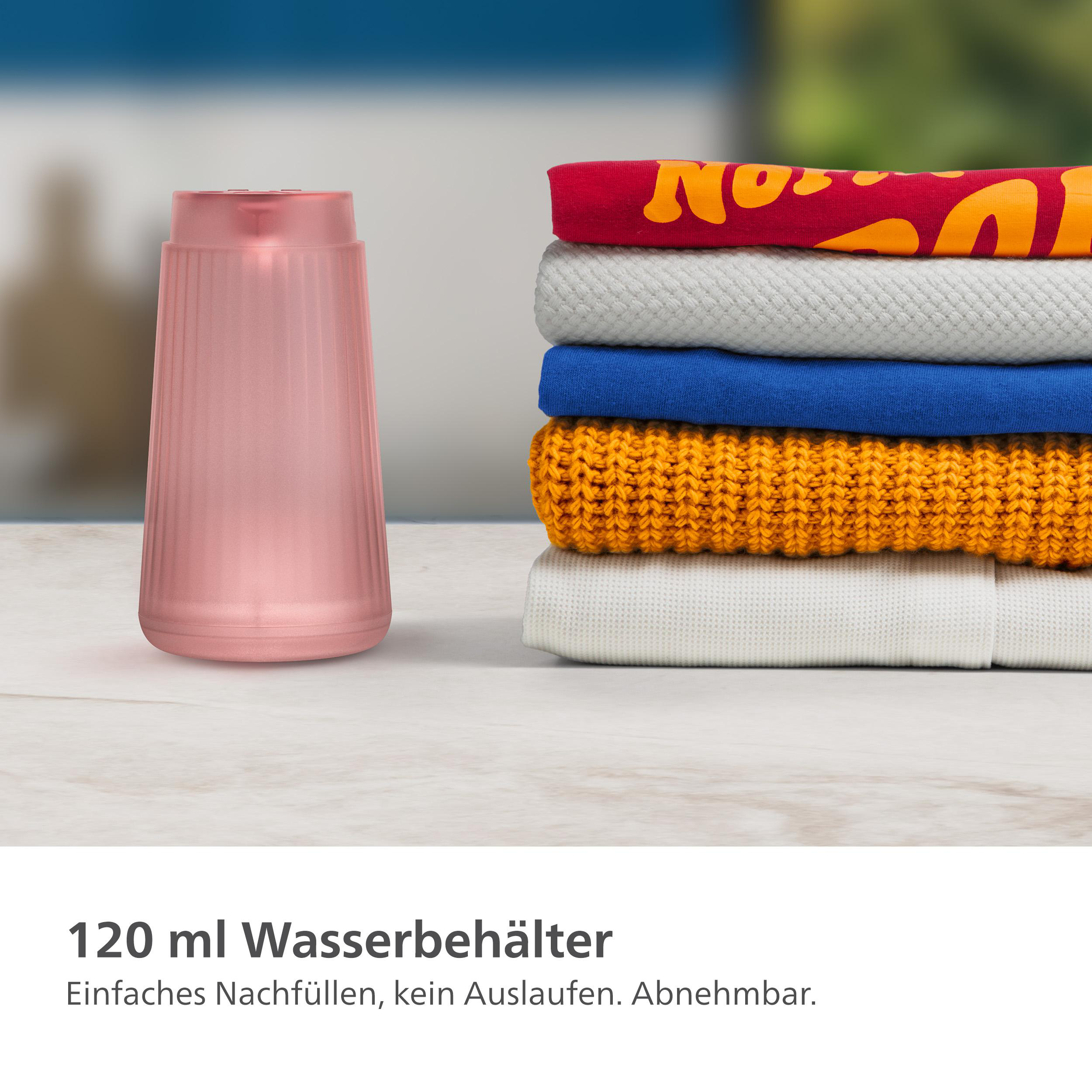 Rosa Diffusor neben einem Stapel gefalteter Kleidung. Text: "120 ml Wasserbehälter", darunter Anweisungen.