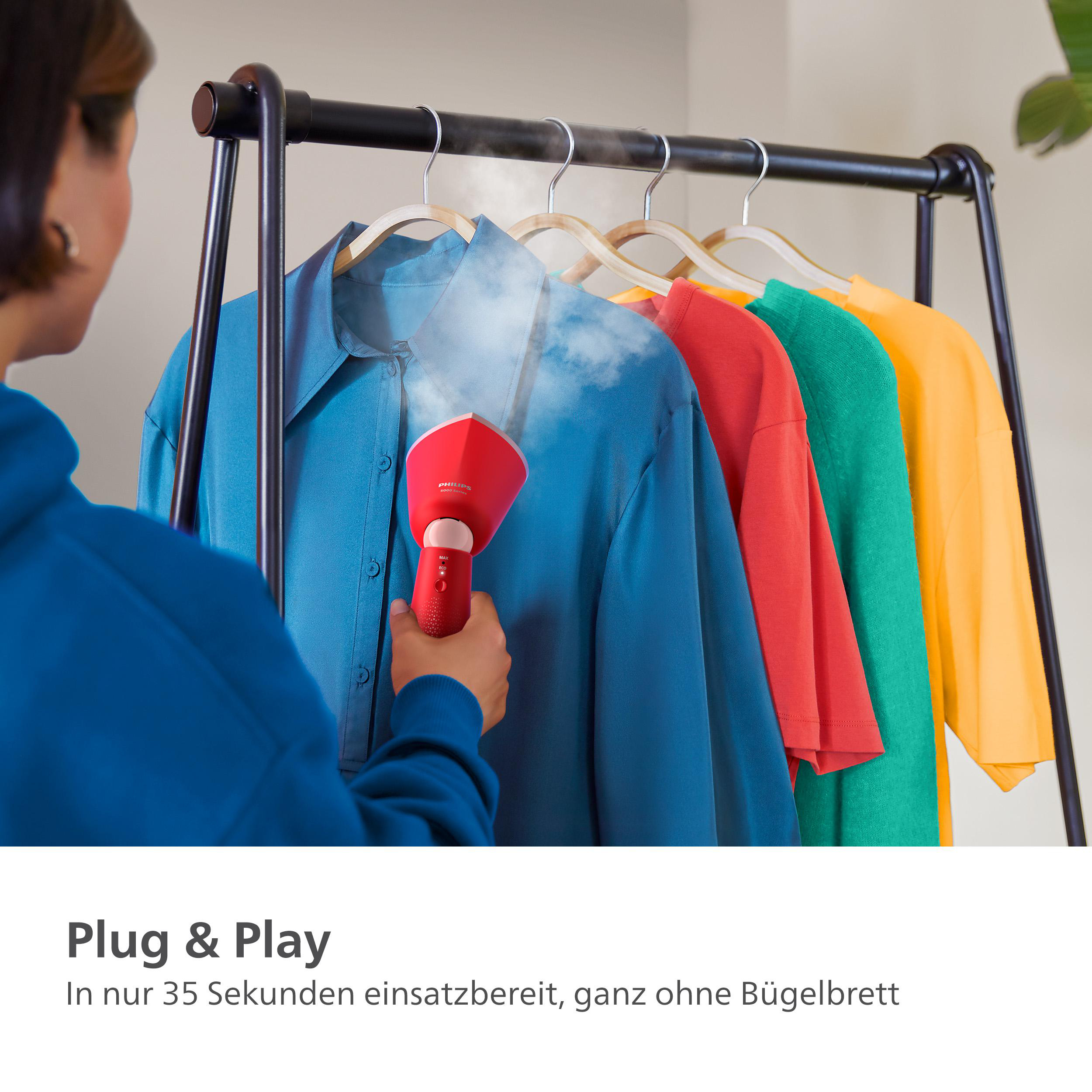 Eine Frau bügelt ein blaues Hemd auf einem Gestell mit anderen bunten Hemden mit einem roten Steamer.