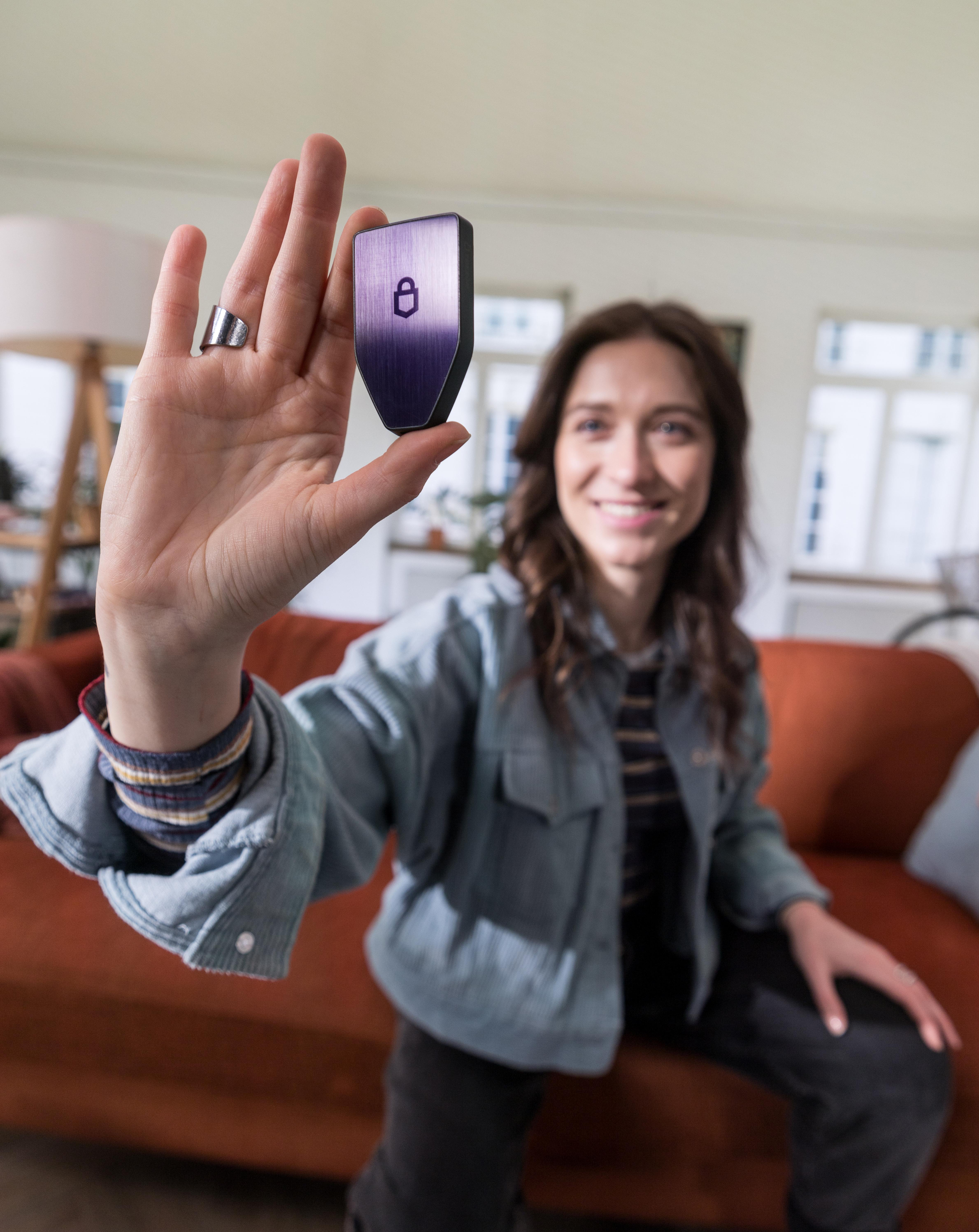 Eine Frau hält ein lila Smart Lock. Sie lächelt und sitzt auf einem orangefarbenen Sofa.