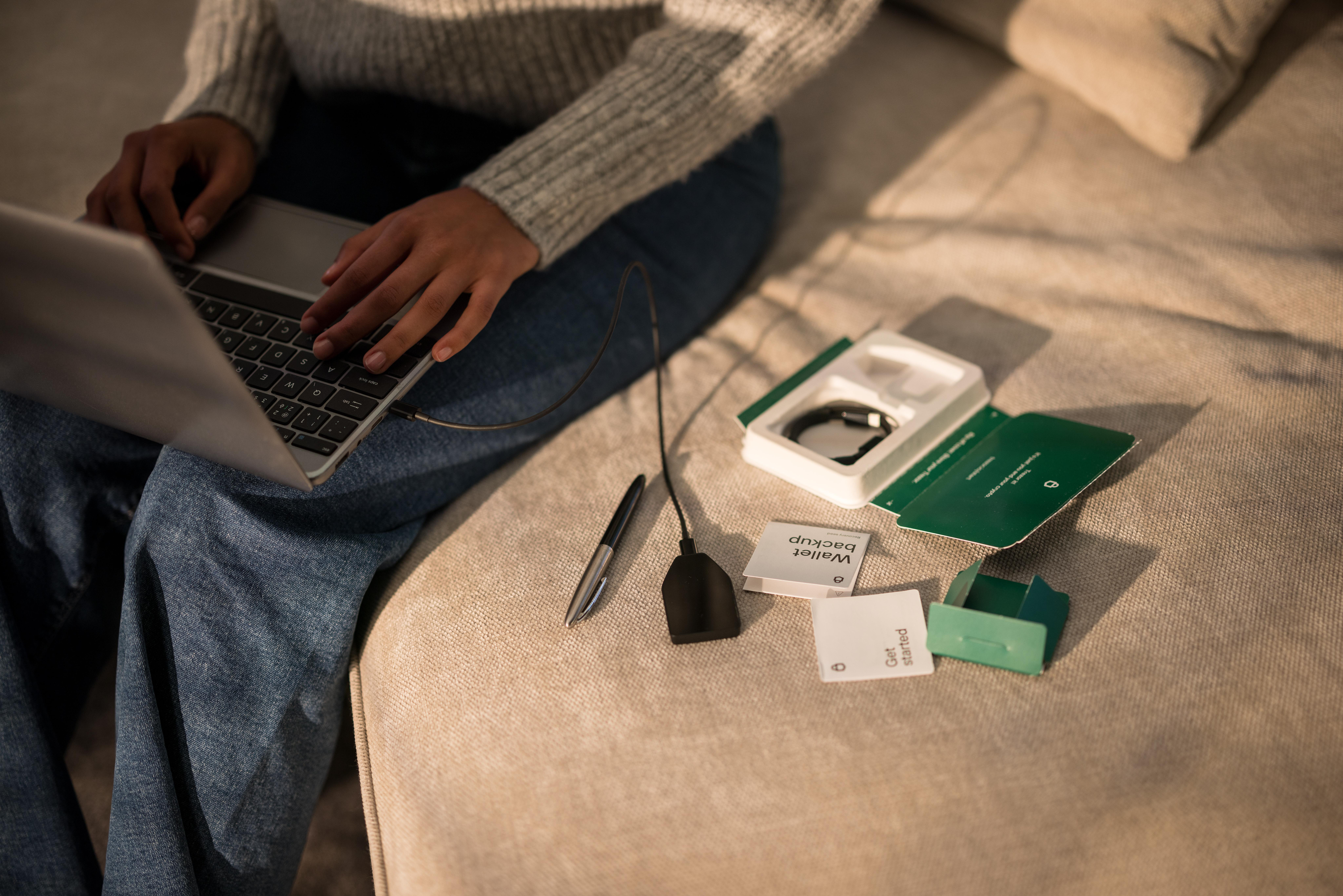 Eine Person nutzt Laptop und Smartwatch-Zubehör auf einem Sofa, Stift und Notizen sichtbar.