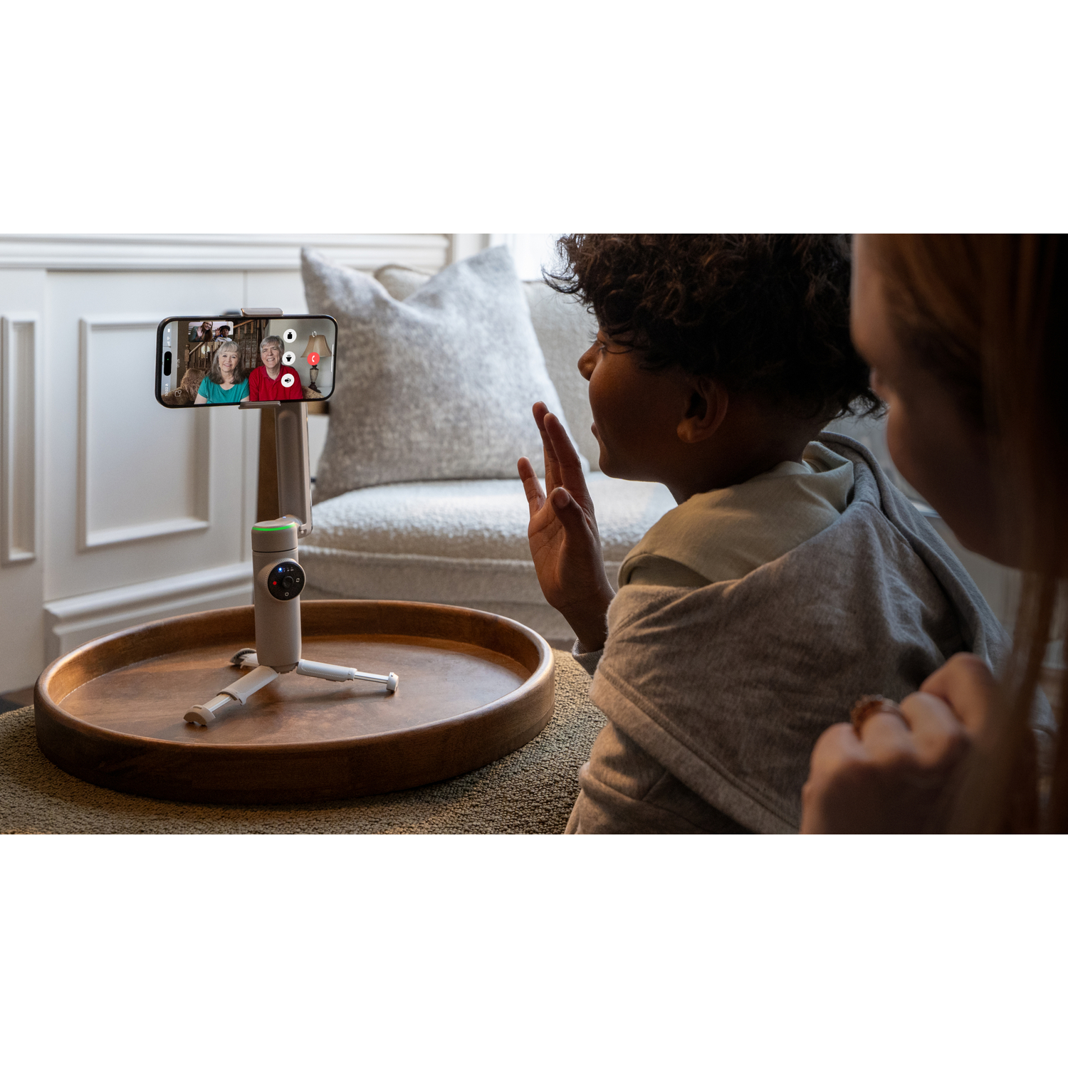 A child video chatting on a phone mounted on a tripod, with a person in the foreground.