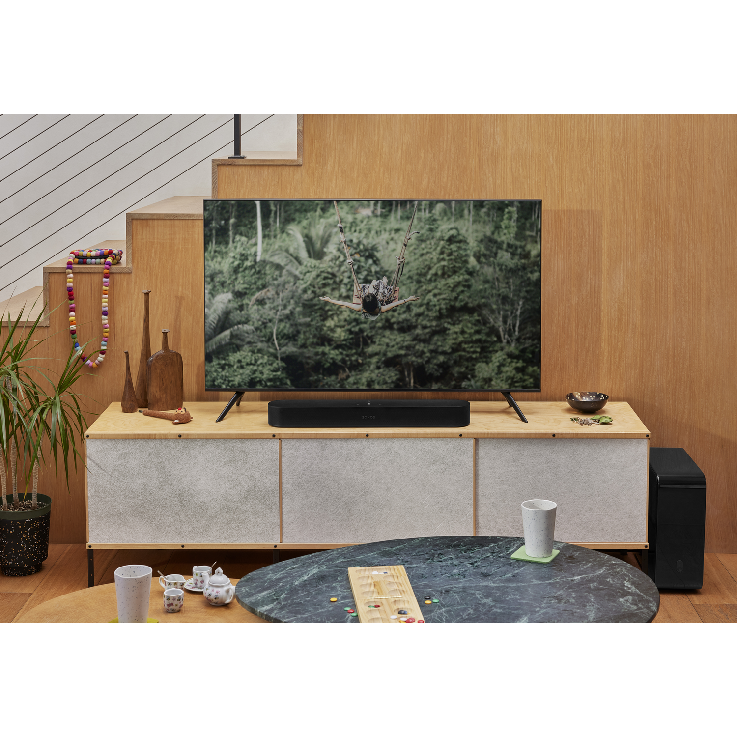 Woonkameropstelling met tv, soundbar en houten meubels. Inclusief een zwarte subwoofer.