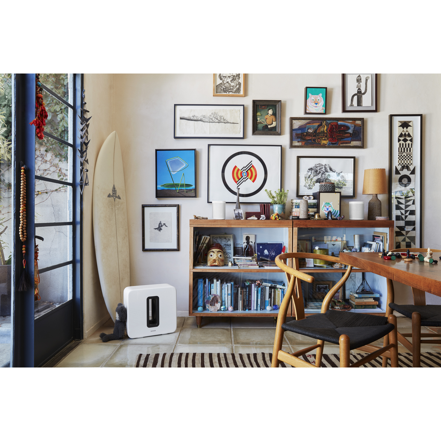 Woonkamer met kunstwerken, een surfplank en een Sonos-luidspreker.