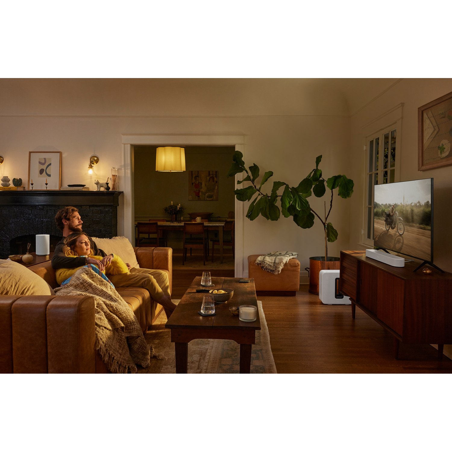 Een stel op een bank kijkt tv in een woonkamer, met een witte luidspreker zichtbaar.