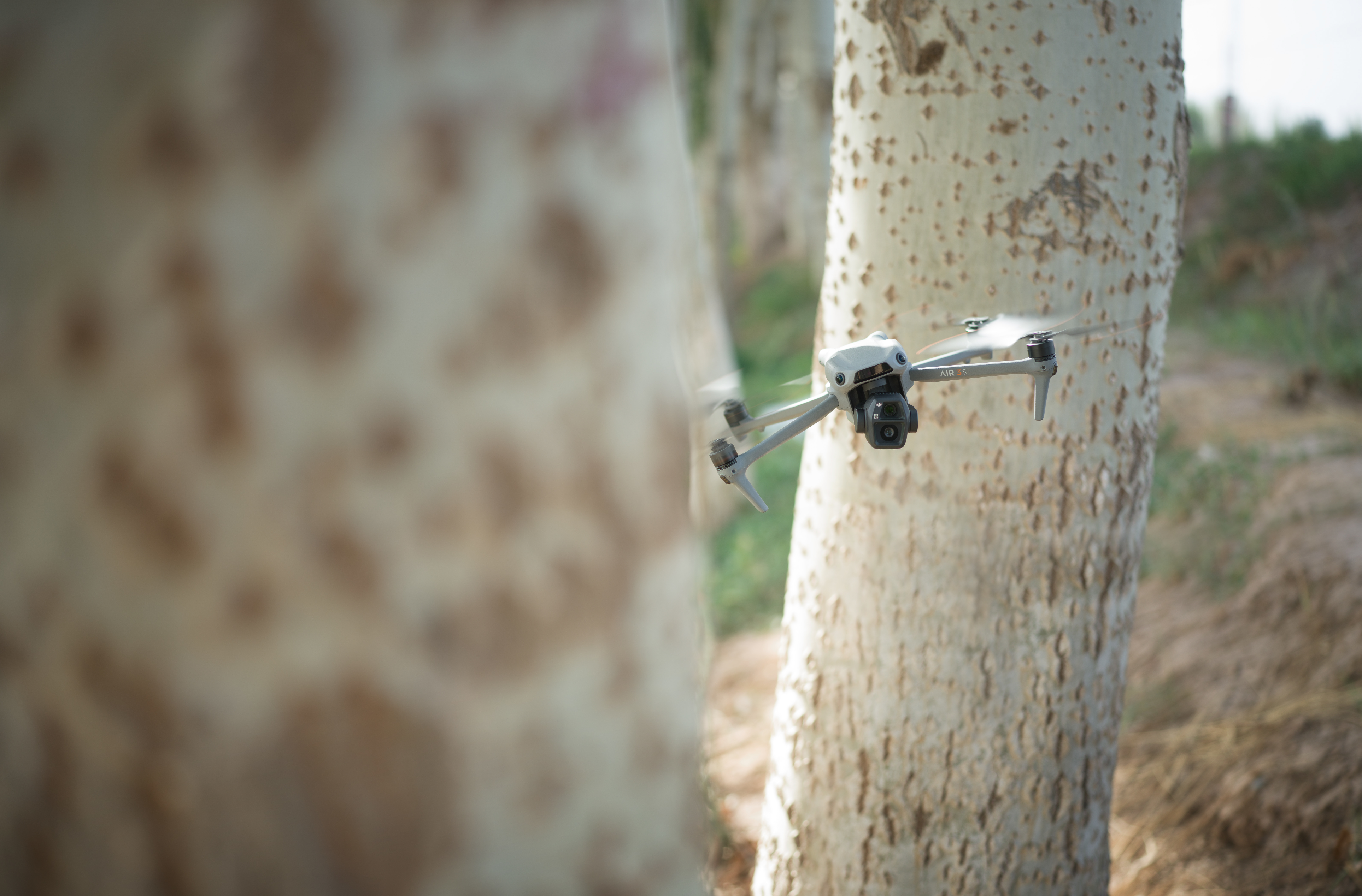 Un drone che vola tra gli alberi con un albero sfocato in primo piano.