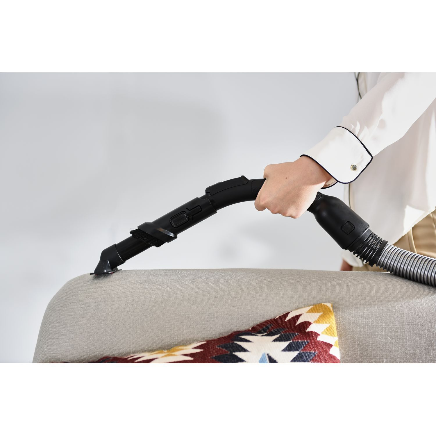 A person's hand vacuuming a grey sofa with a black nozzle.