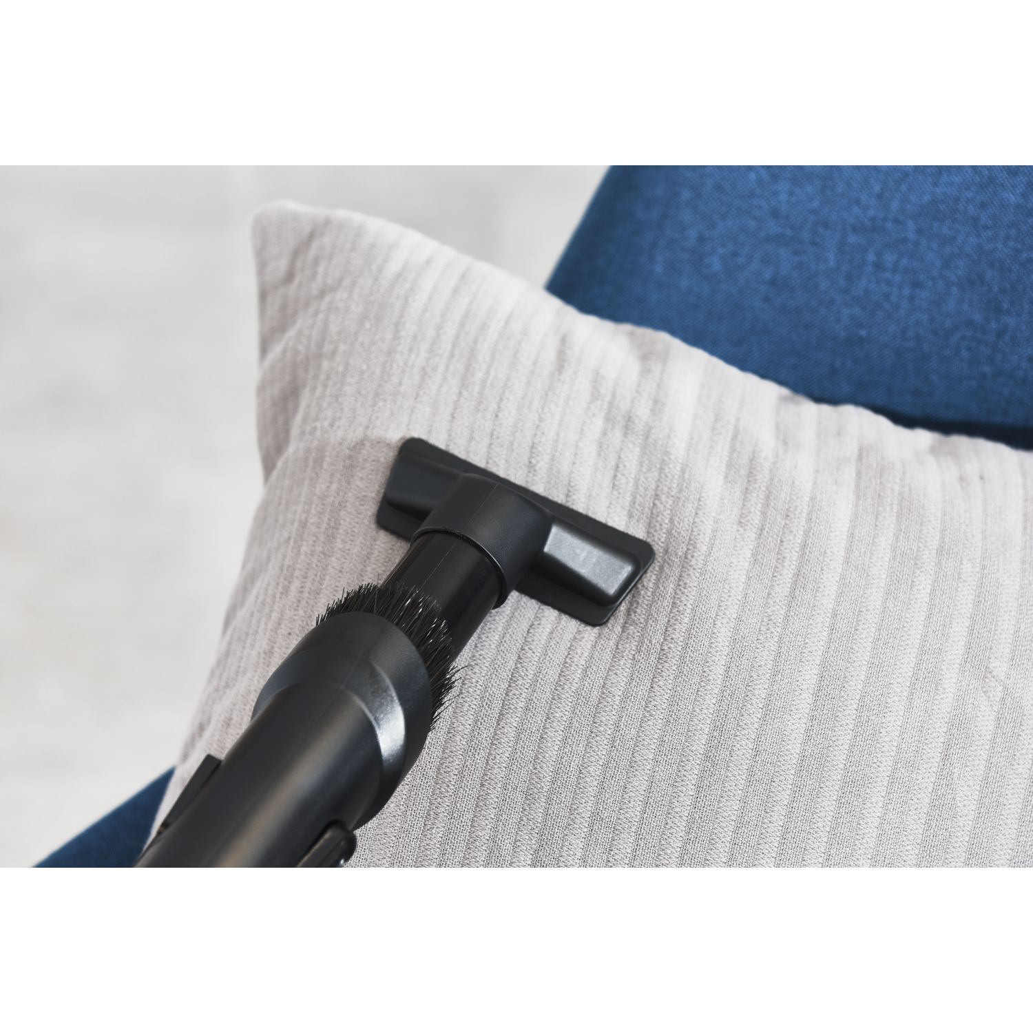 A black vacuum cleaner nozzle cleaning a light gray striped pillow.