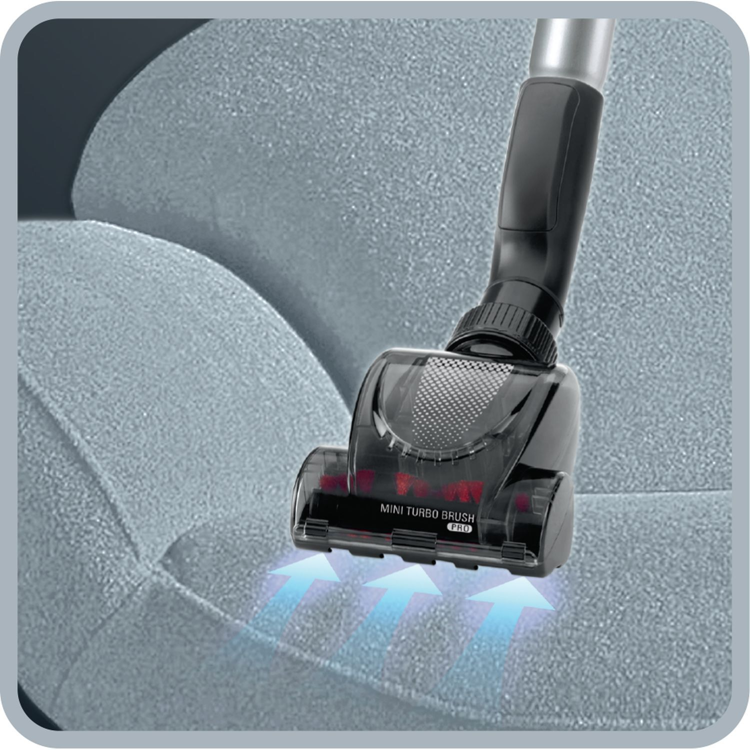 Close up of a black mini turbo brush vacuuming a blue sofa. Arrows indicate suction direction.