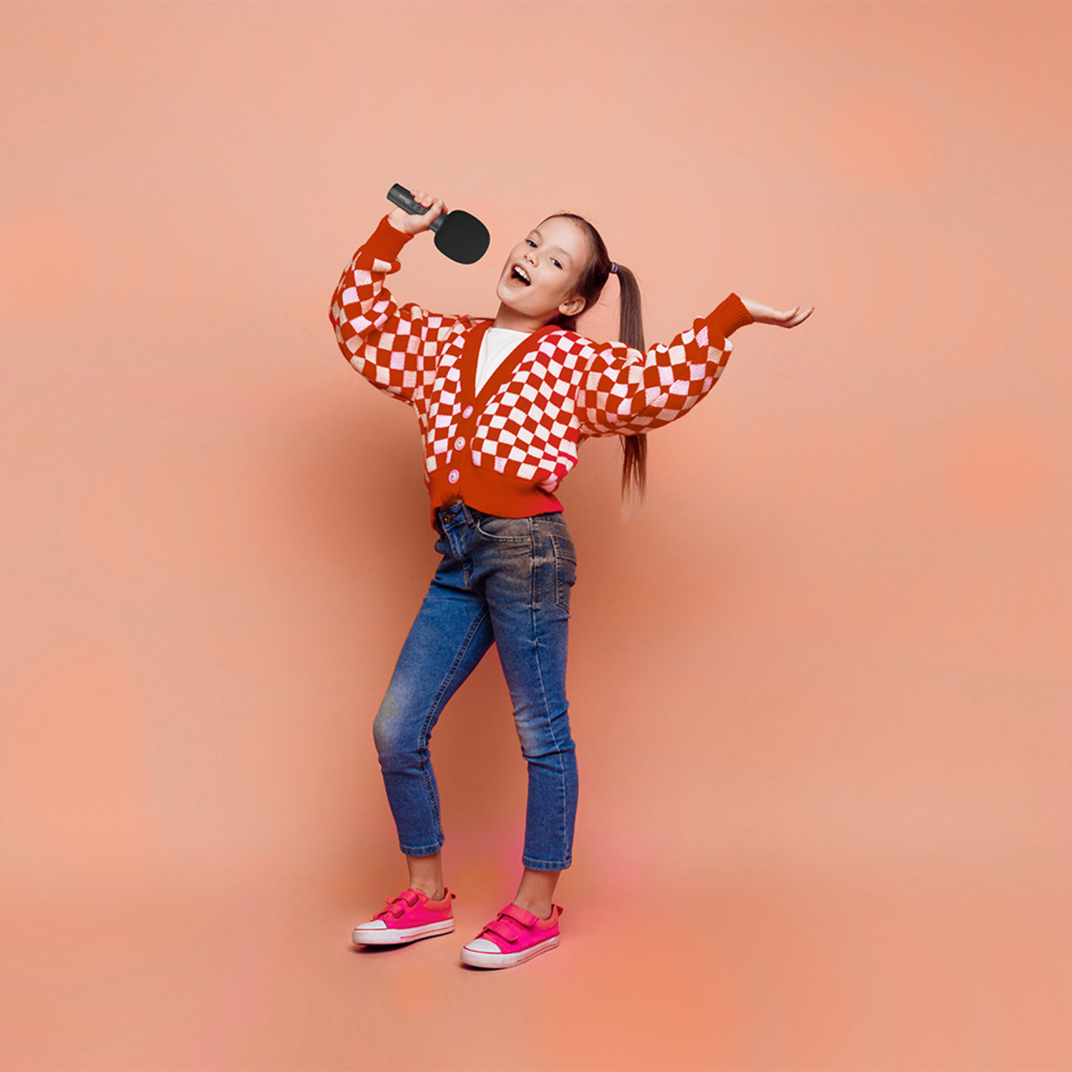 Girl singing into a black microphone, wearing red checkered sweater and jeans.