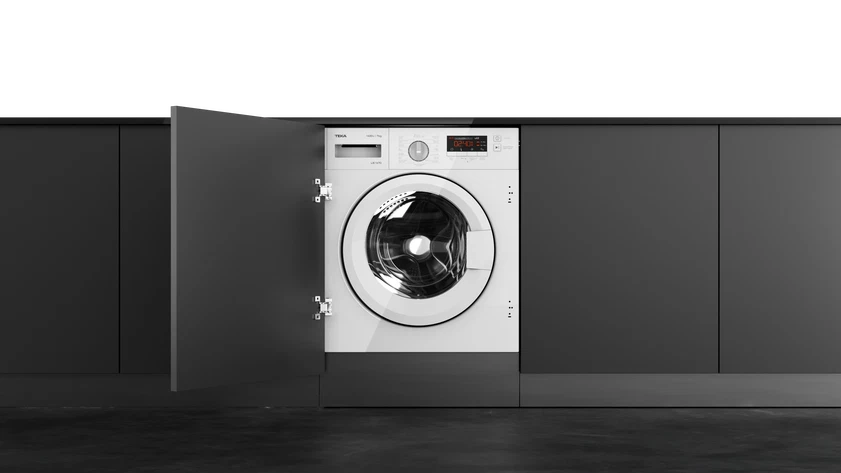 Una lavadora blanca está integrada en un armario gris oscuro, con una puerta abierta.