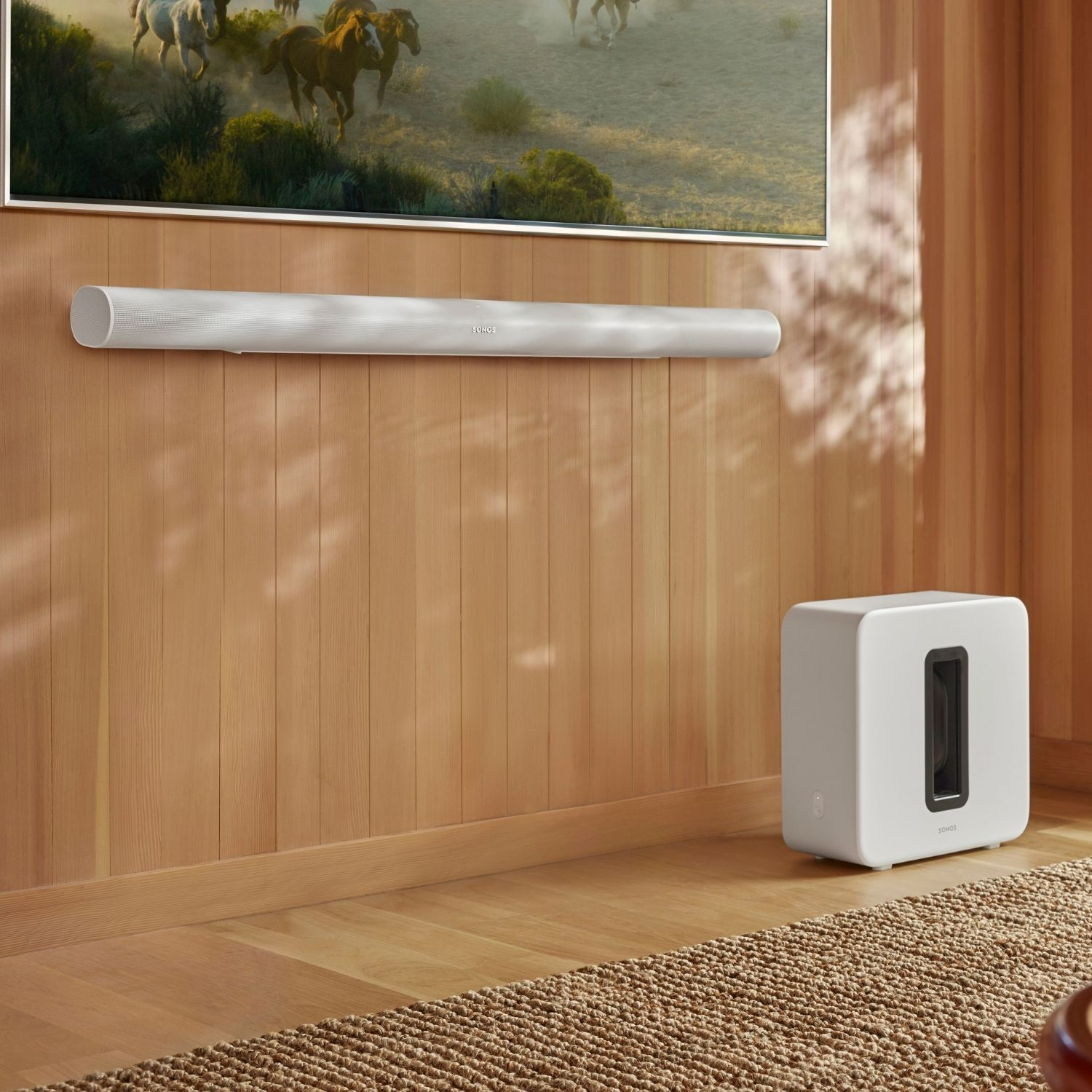 Una barra de sonido blanca sobre un subwoofer blanco, montado en una pared de madera.